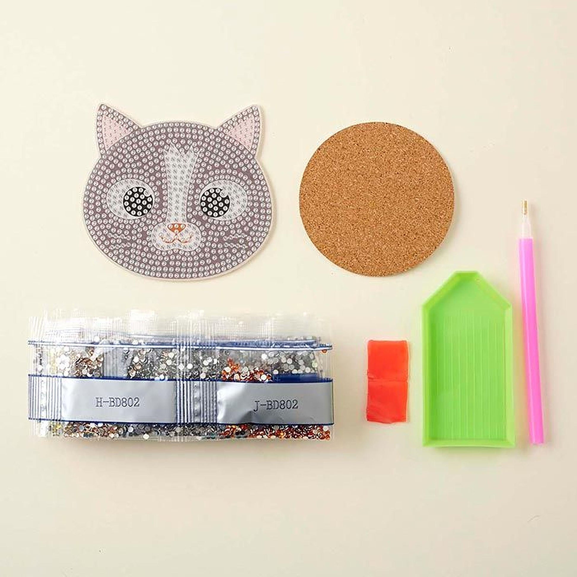 various craft supplies, including a cat-shaped object, a cork coaster, a pen, a small bag of rhinestones, a red object, and a green object.