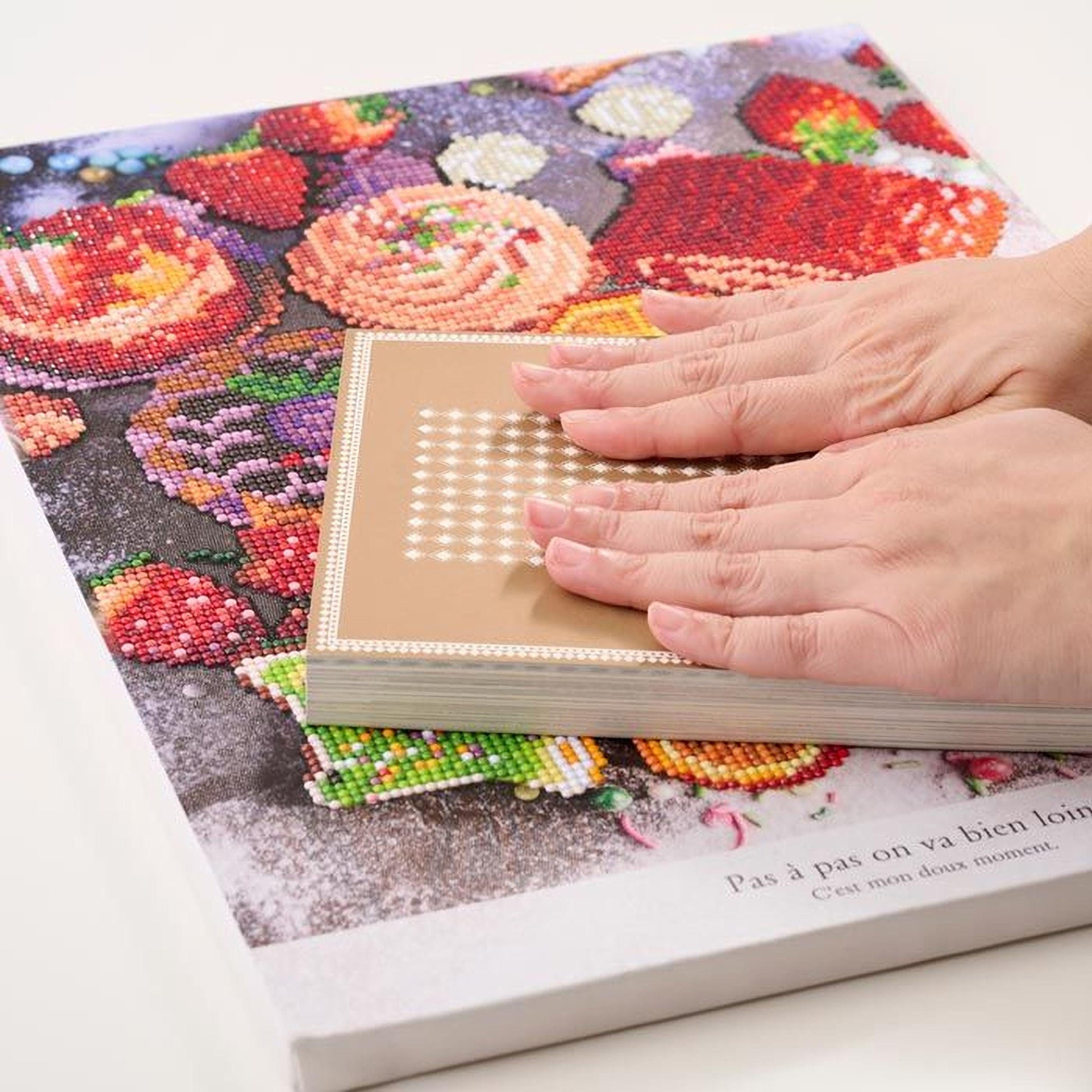 A person's hands are holding a book with a colorful, diamond-studded cover featuring a variety of fruits and flowers.
