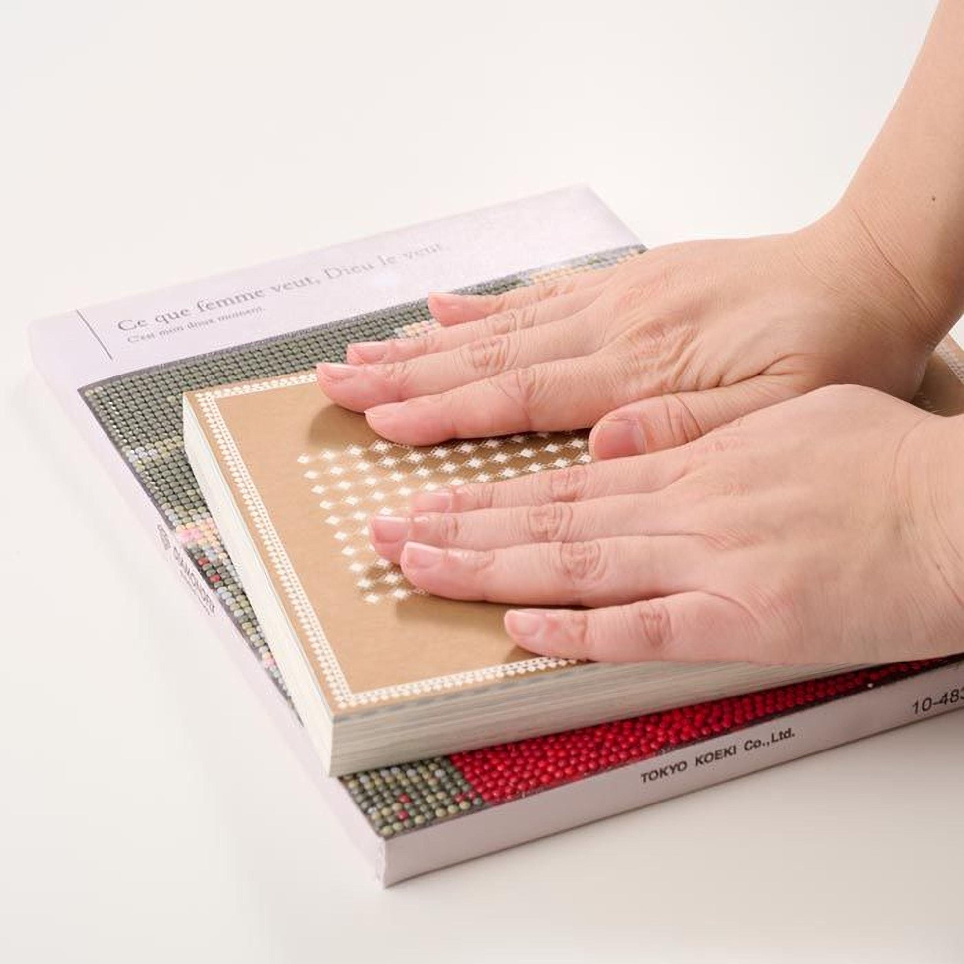 A person's hands are holding a book with a patterned cover, resting on top of another book.