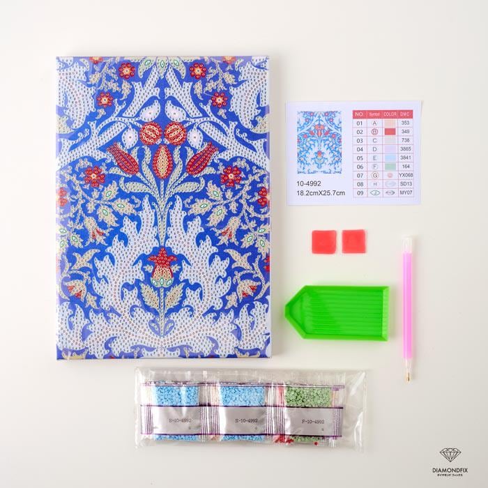 various craft supplies, including a notebook with a blue and white floral pattern, a diamond-patterned pen, a green diamond-patterned tool, and a package of colorful beads.