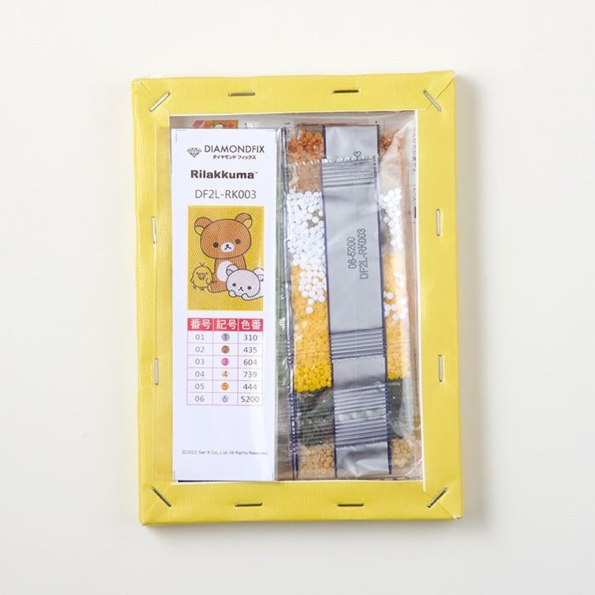 a yellow frame with a label and a clear plastic bag containing colorful beads or grains, possibly for a craft or art project.