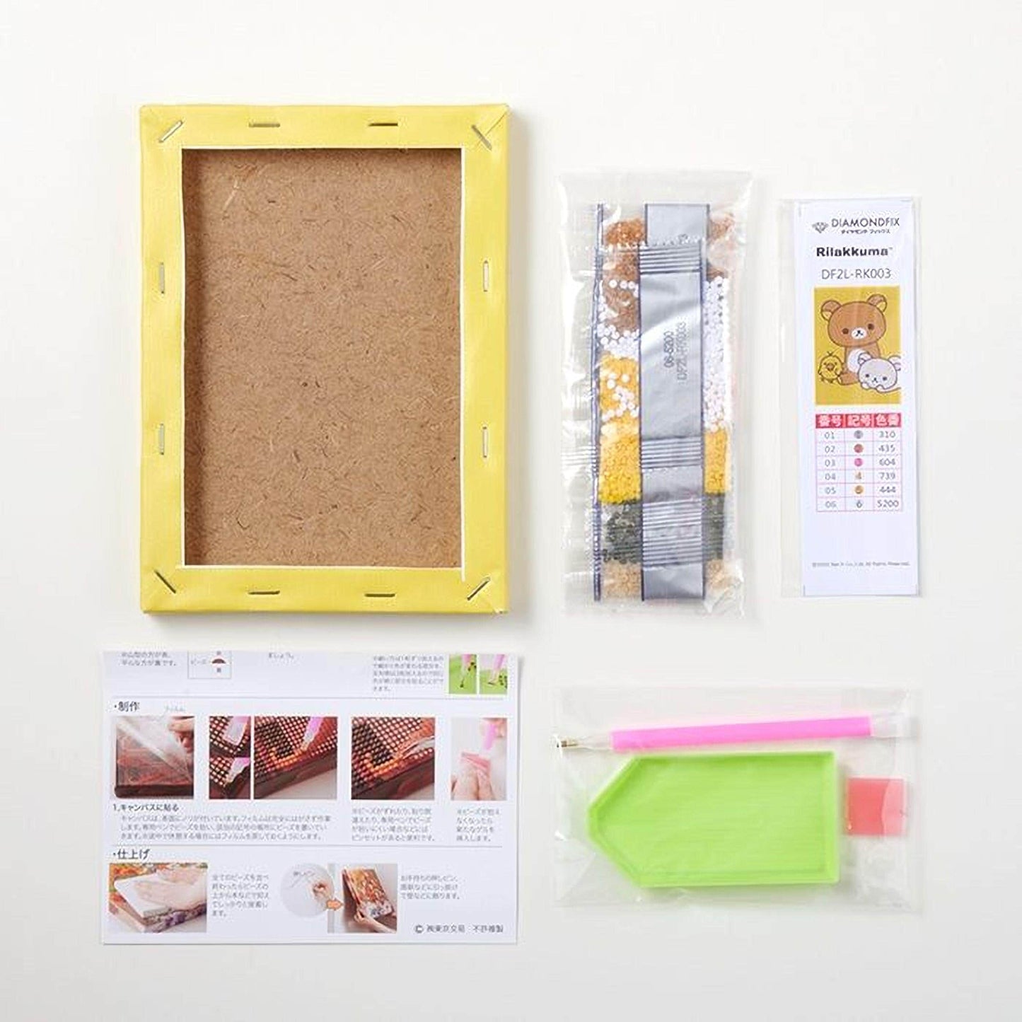 various craft supplies, including a yellow frame, a package of diamond-encrusted paper, a diamond-encrusted pencil, and a diamond-encrusted pen. There is also a booklet with instructions and images, as well as a small green and pink tool.