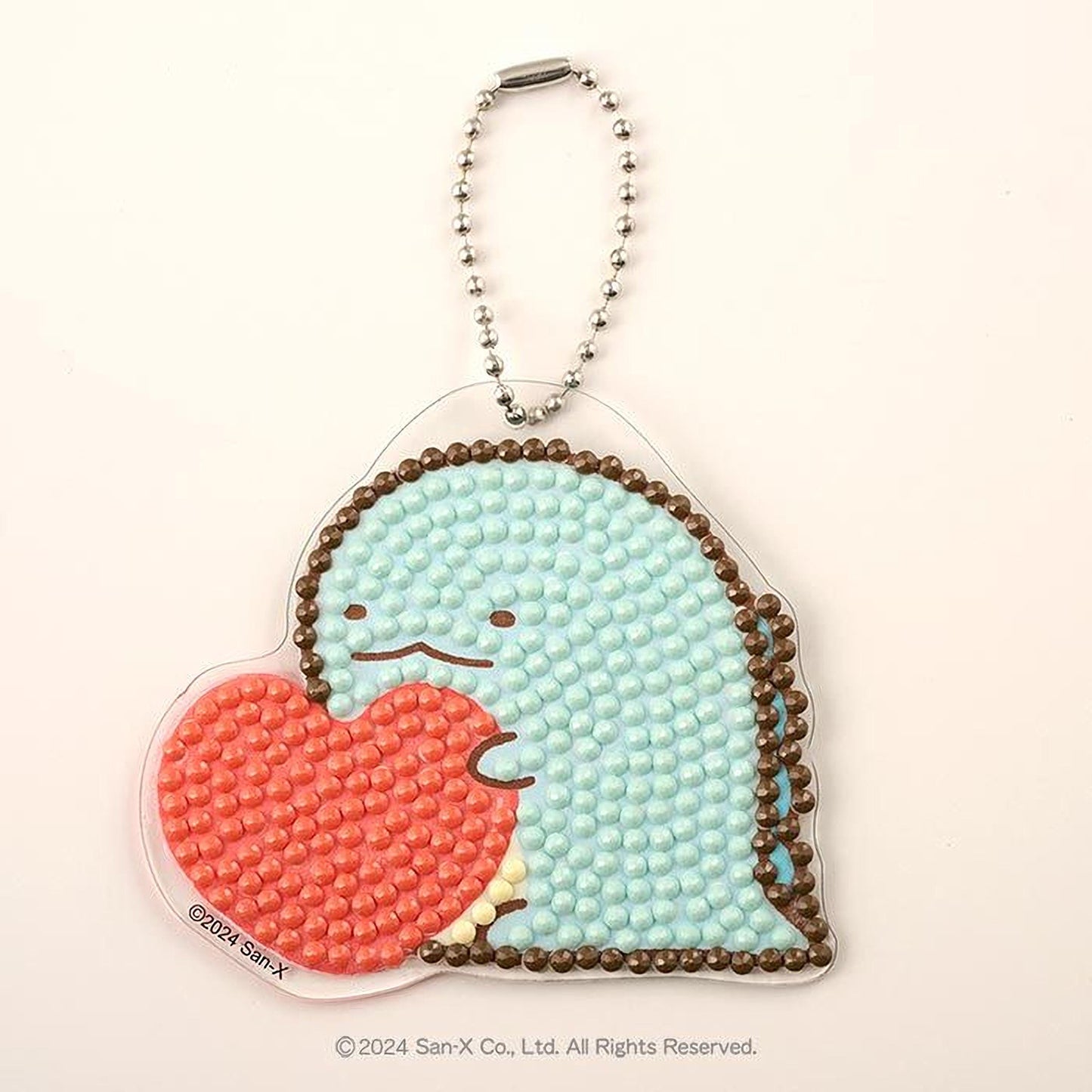 A heart-shaped pendant with a chain attached to it, featuring a small blue dinosaur-like character holding a red heart.