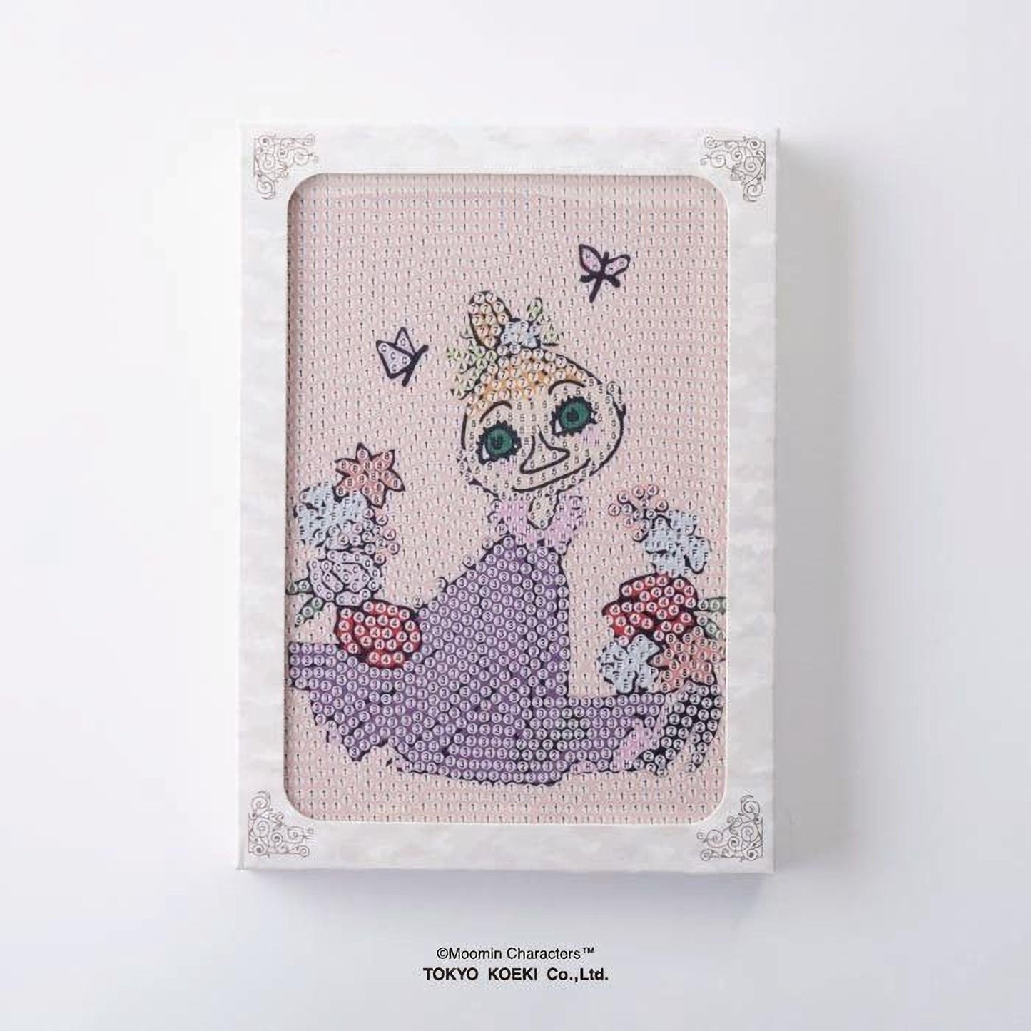A framed embroidered image depicting a cartoon character surrounded by flowers and butterflies.