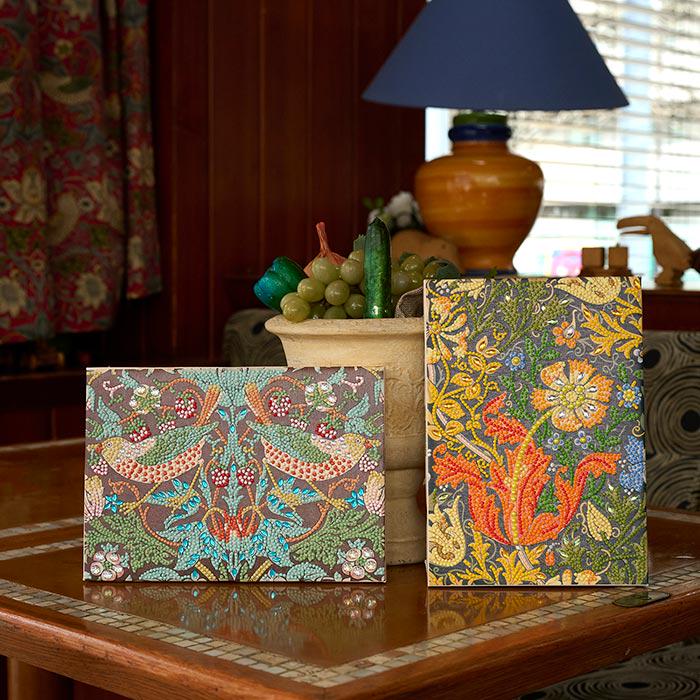 two framed artworks with intricate floral designs, placed on a wooden table.