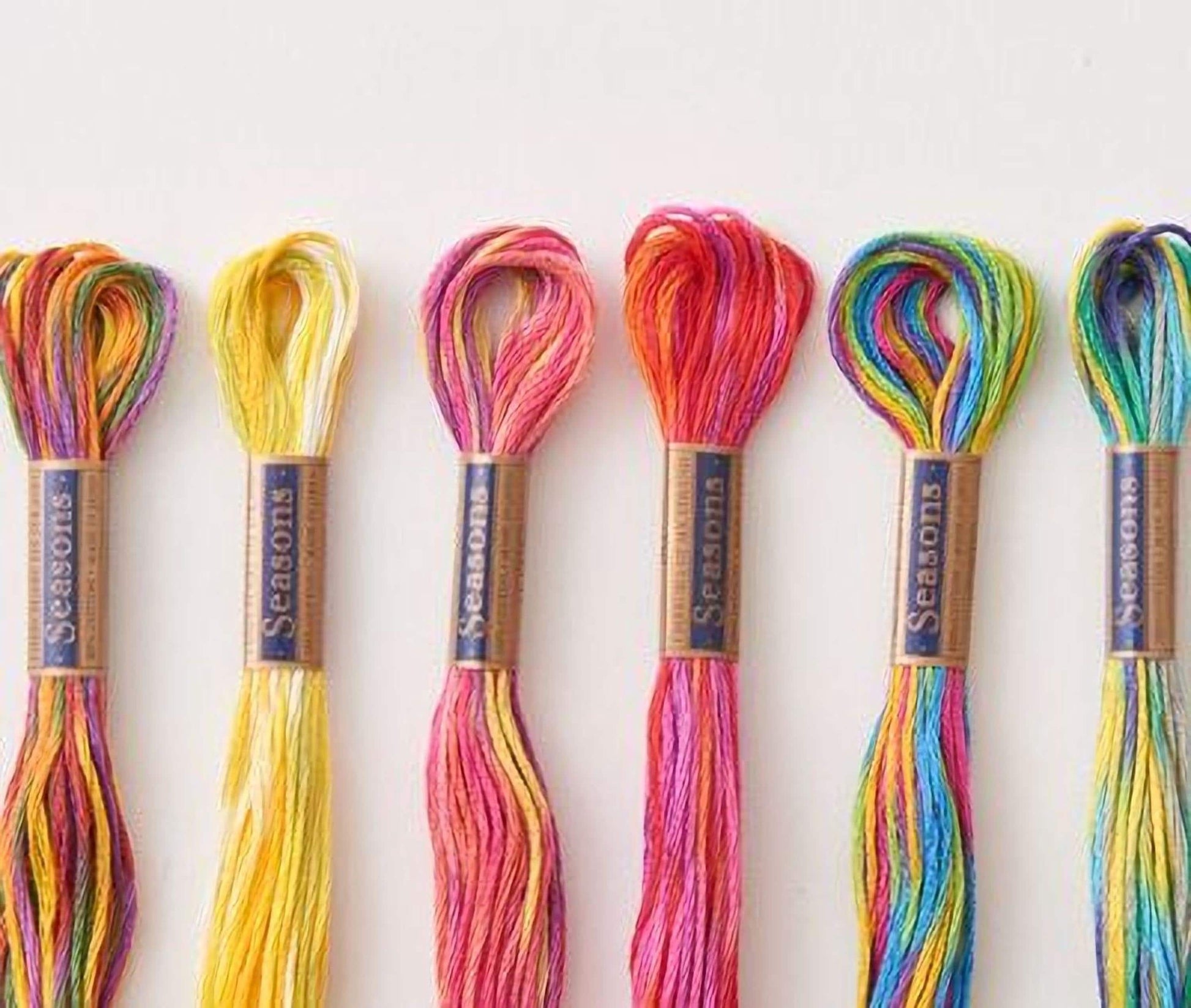 A collection of six colorful spools of thread, each with a label that reads "Seasons", arranged in a row.