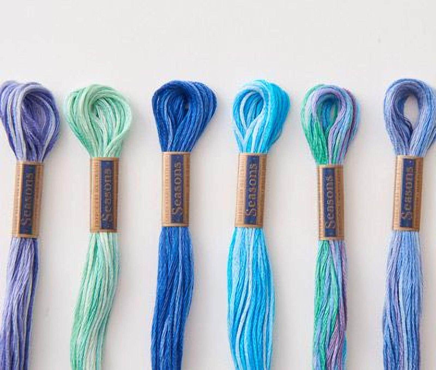 A collection of six spools of thread in various colors, including blue, green, and purple, arranged in a row.