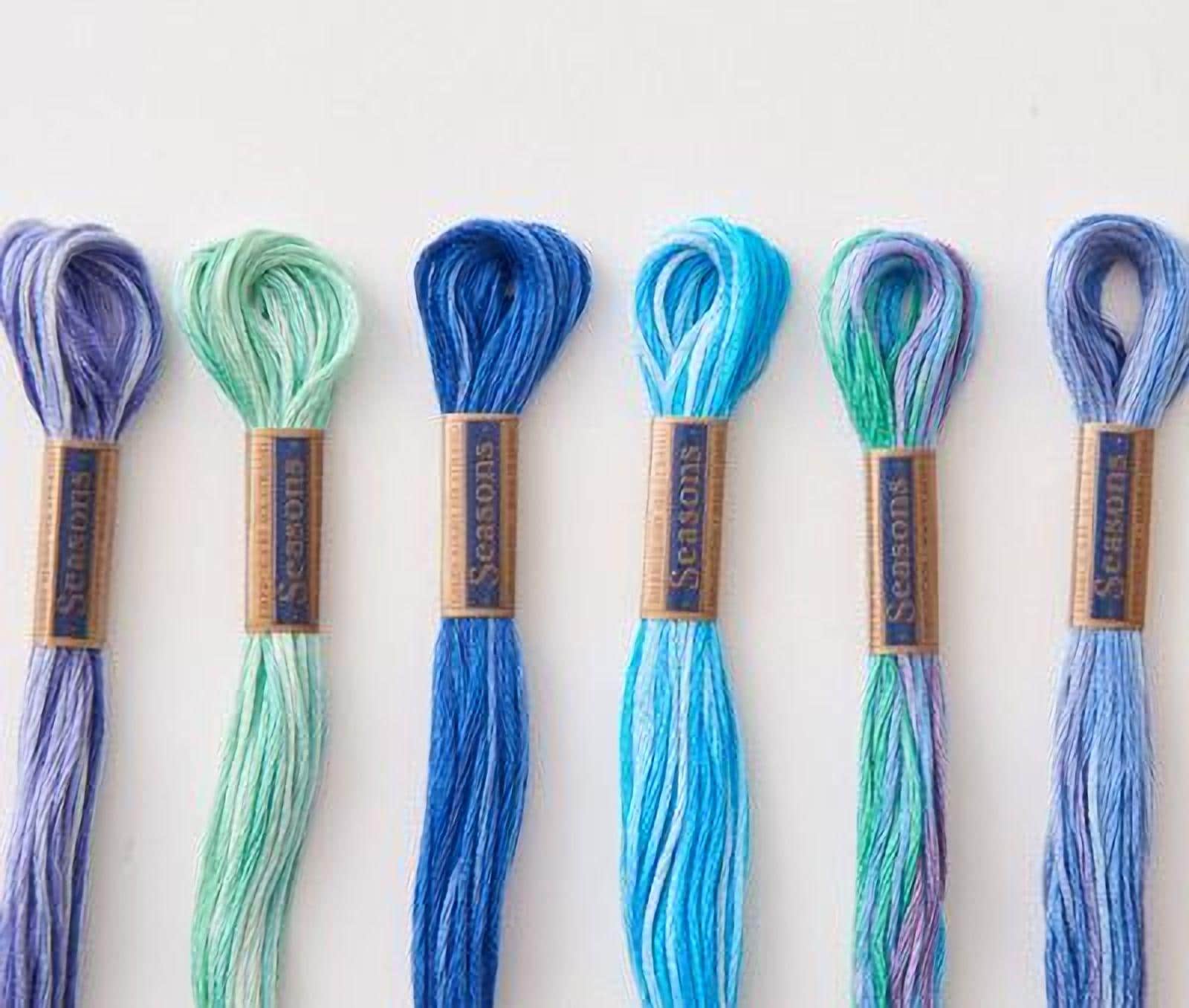 A collection of six spools of thread in various colors, including blue, green, and purple, arranged in a row.