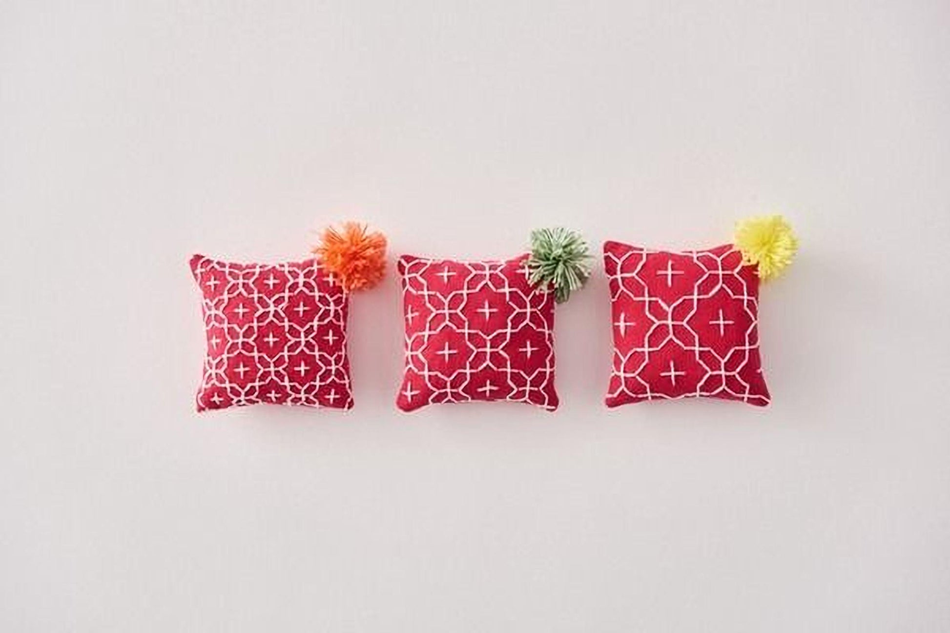 Three red and white patterned pillows with pom-poms are arranged in a row on a white background.