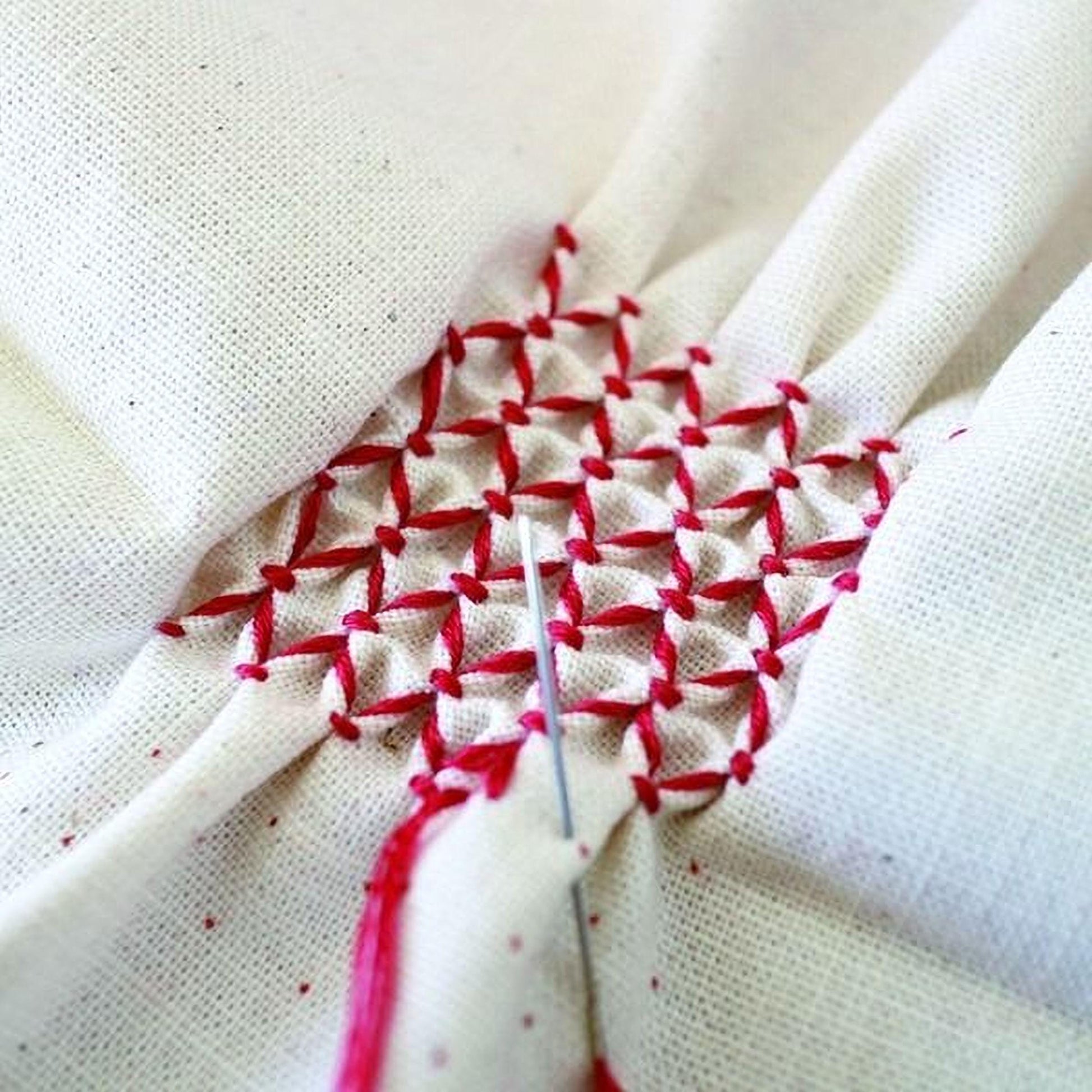 a close-up view of a hand-stitched fabric with a red and white pattern, featuring a diagonal grid of red stitches.