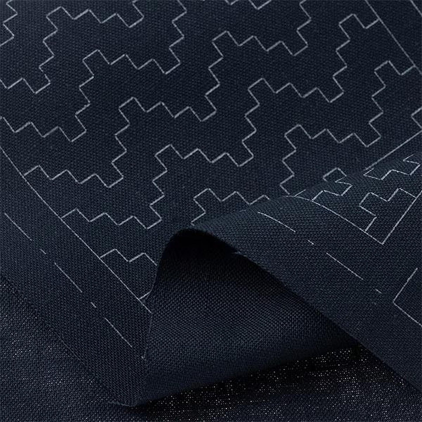 a close-up view of a dark fabric with a repeating geometric pattern in white. The pattern consists of various shapes and lines, creating a visually striking and intricate design.