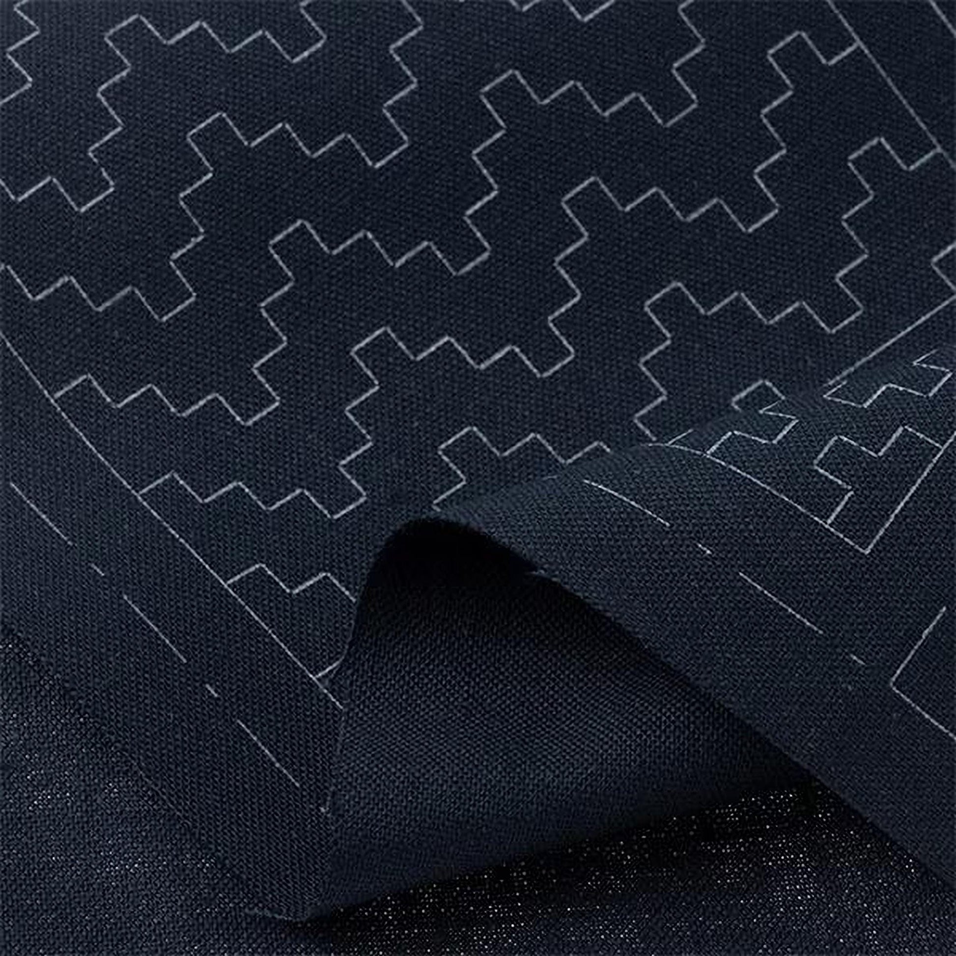 a close-up view of a dark fabric with a repeating geometric pattern in white. The pattern consists of various shapes and lines, creating a visually striking and intricate design.