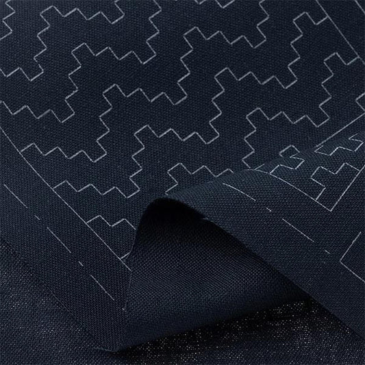 a close-up view of a dark fabric with a repeating geometric pattern in white. The pattern consists of various shapes and lines, creating a visually striking and intricate design.