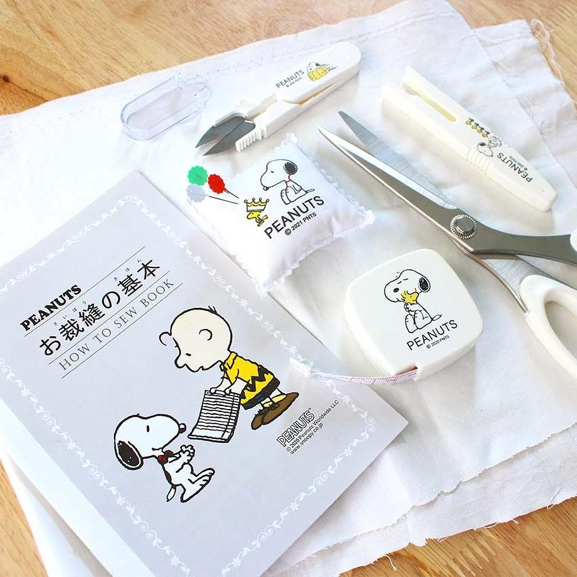 A sewing kit containing various sewing tools and a book with illustrations of characters from the Peanuts comic strip.