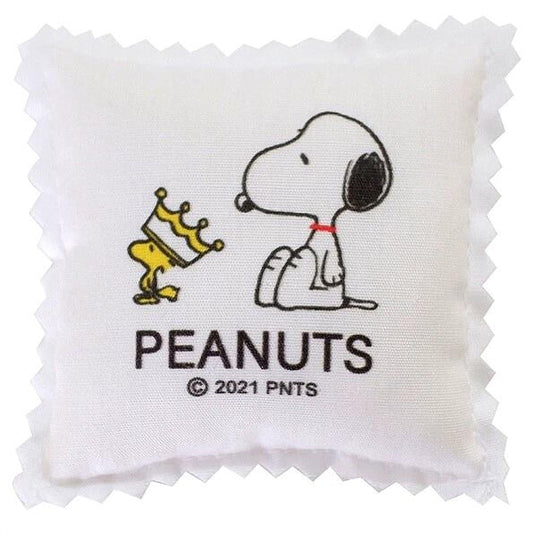 A white square pillow with a cartoon image of a dog wearing a crown and the text "PEANUTS" below it.