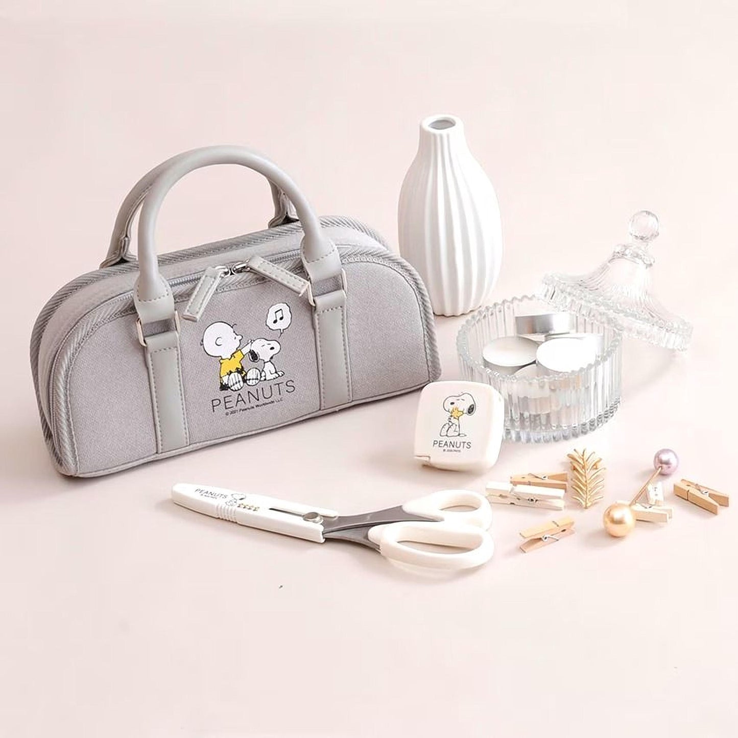 a gray Peanuts-themed bag, a pair of scissors, a white vase, and various other items such as a small glass container, pearls, and clothespins.