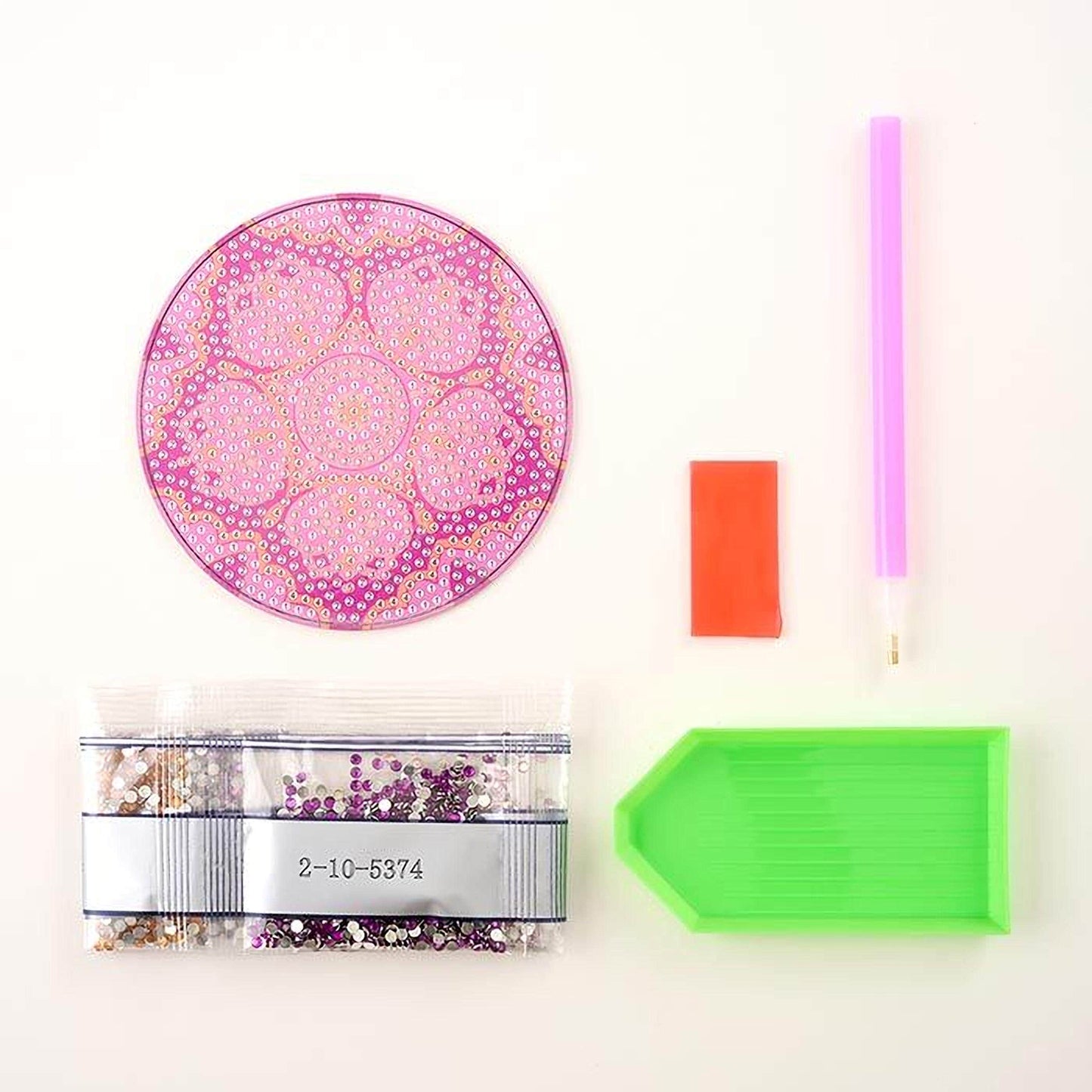 various craft supplies, including a pink and purple flower-patterned mat, a green and orange stamp, a purple pen, a clear plastic bag filled with glittery material, and a green diamond-patterned tool.