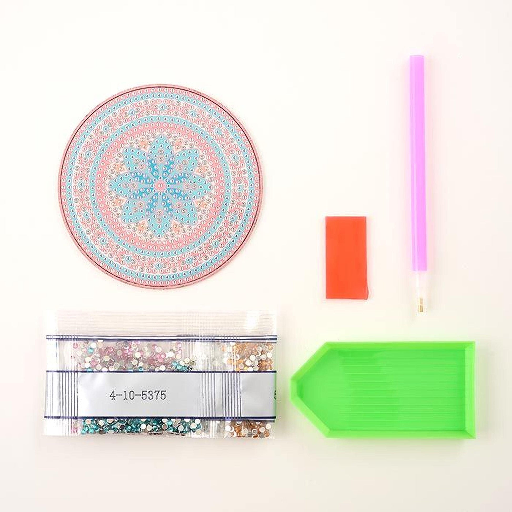 a variety of craft supplies, including a pink pen, a green diamond tool, a bag of glitter, and a small red object.