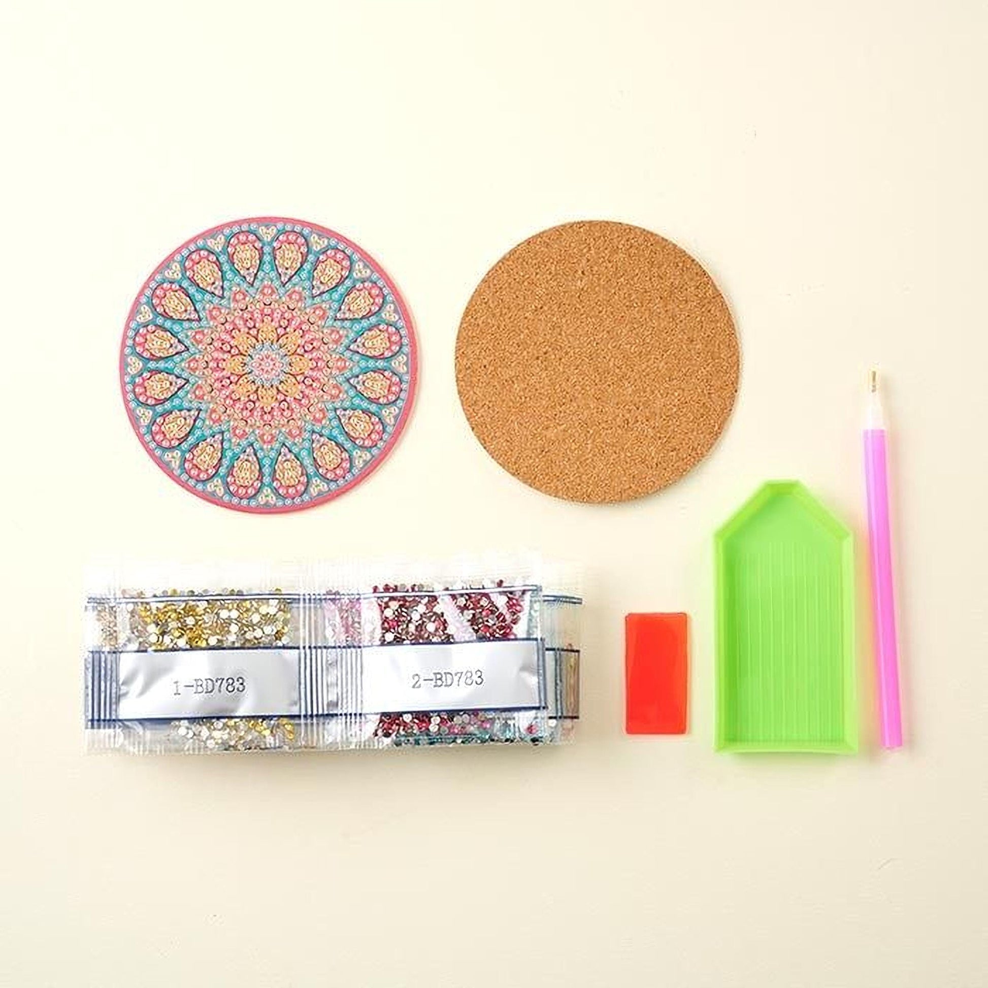 various craft supplies, including a cork coaster, a pen, a package of rhinestones, a clear plastic tray, and a diamond tool.