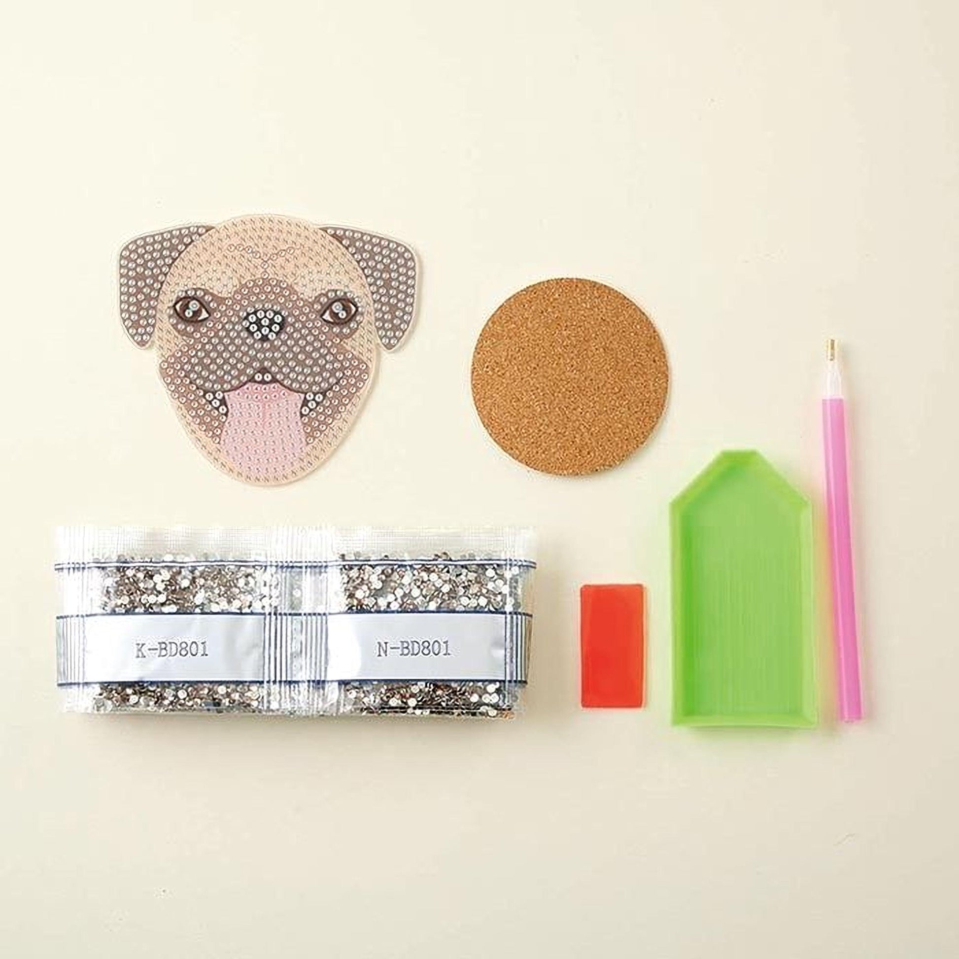 various craft supplies, including a pug-shaped sticker, a cork coaster, a pen, a small red object, and a green plastic container.