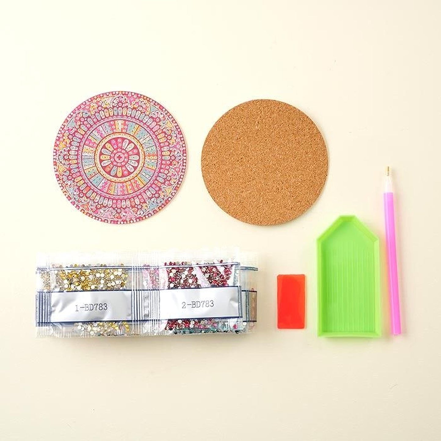 various craft supplies, including a cork coaster, a pen, a package of glitter, and a diamond tool.