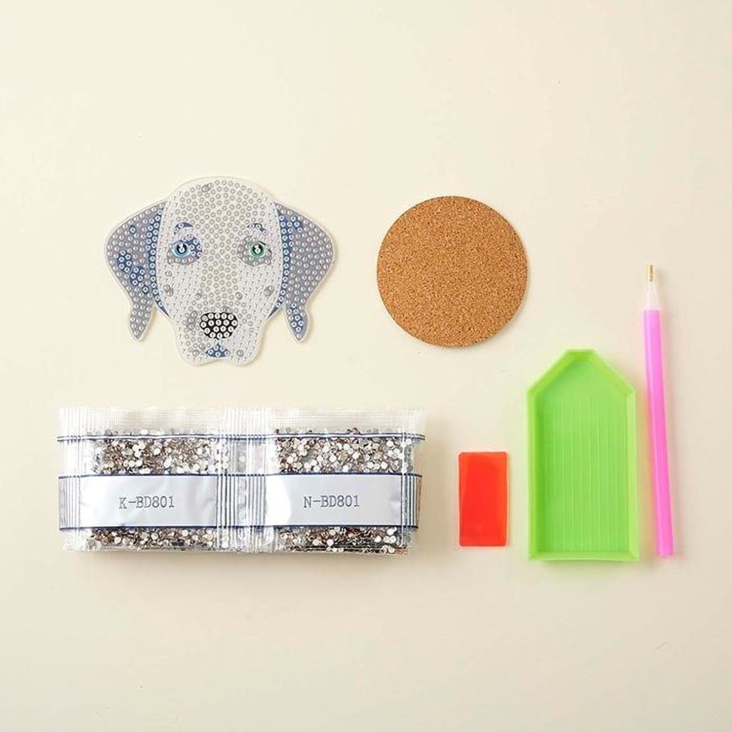 various craft supplies, including a dog-shaped embroidery piece, a cork coaster, a pen, a small red object, and a green diamond tool.