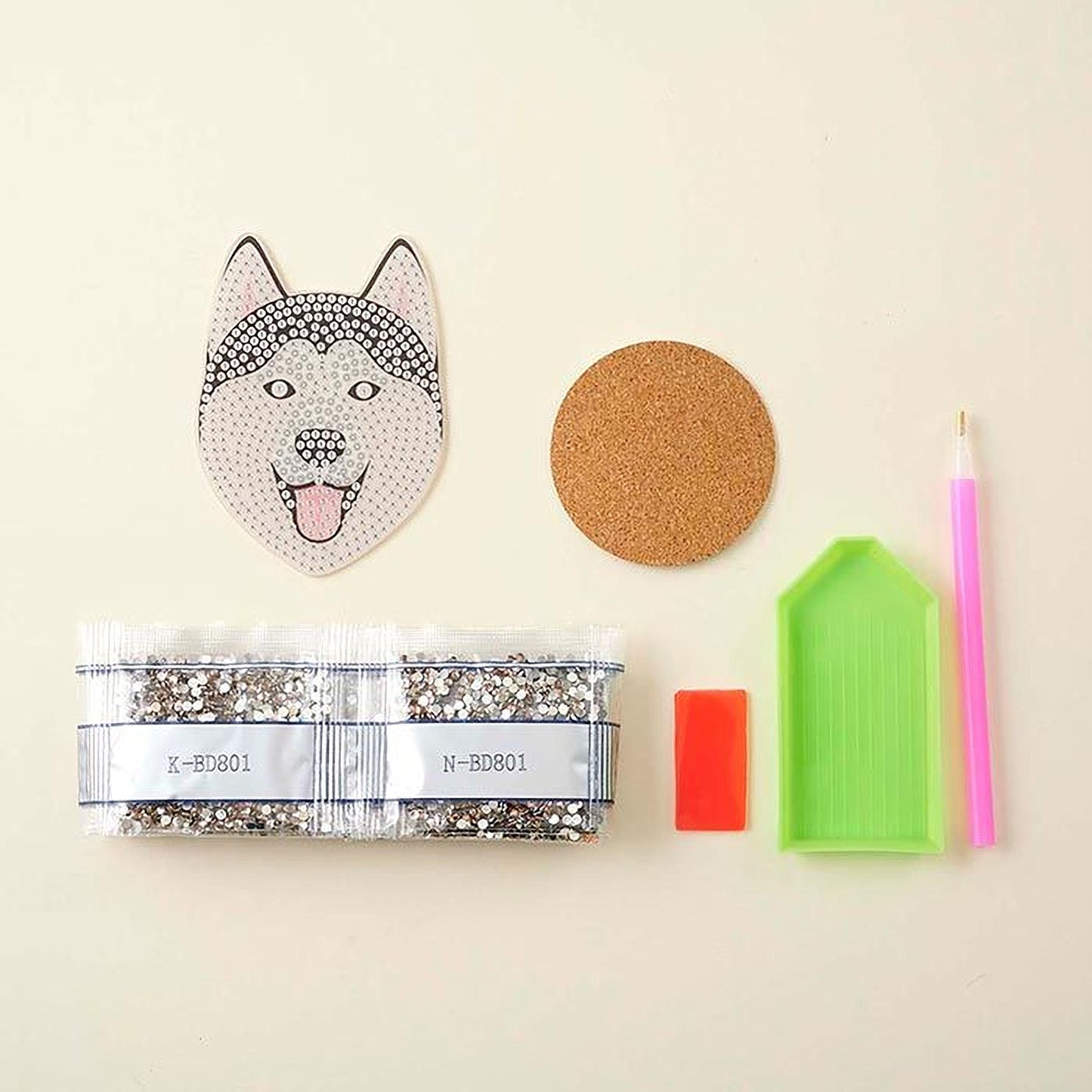 various craft supplies, including a package of rhinestones, a cork coaster, a pen, a small green tray, and a small red object.