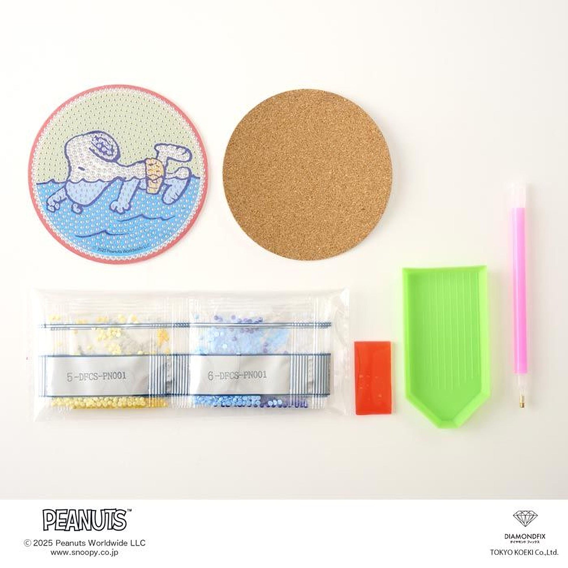 various craft supplies, including a cork coaster, a pen, a plastic bag filled with colorful beads, a diamond grinder, and a small green tray.