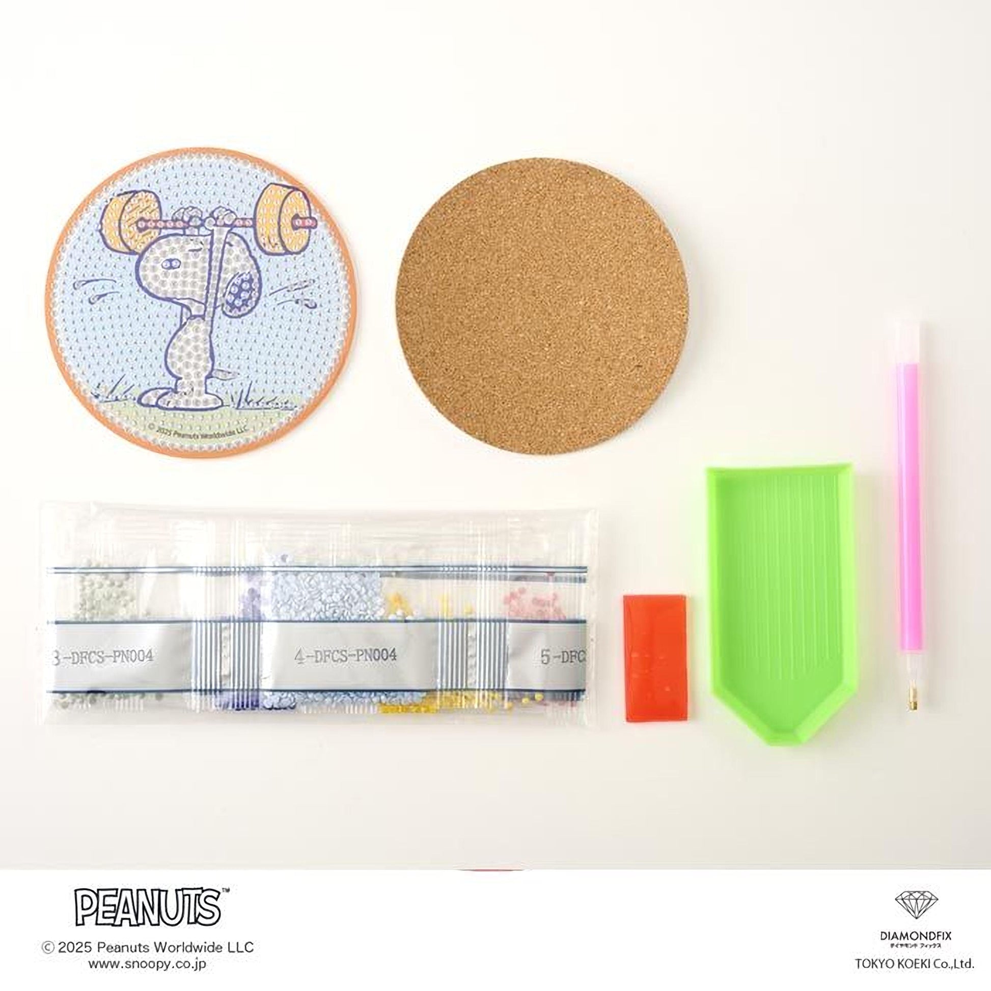 various items related to the Peanuts comic strip, including a round coaster with a cartoon image of a character, a cork coaster, a pen, a green plastic tool, and a package of pebbles.
