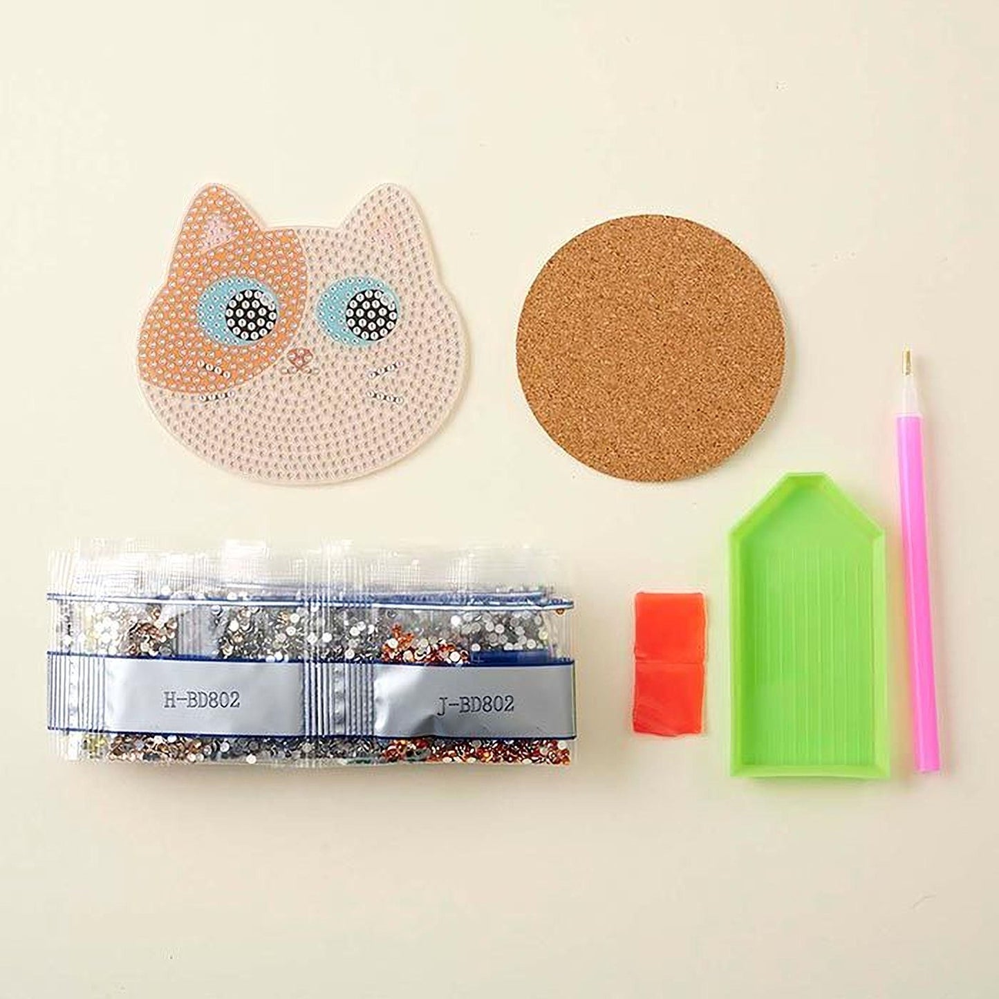 various craft supplies, including a cat-shaped object, a cork coaster, a pen, a bag of rhinestones, and a diamond tool.