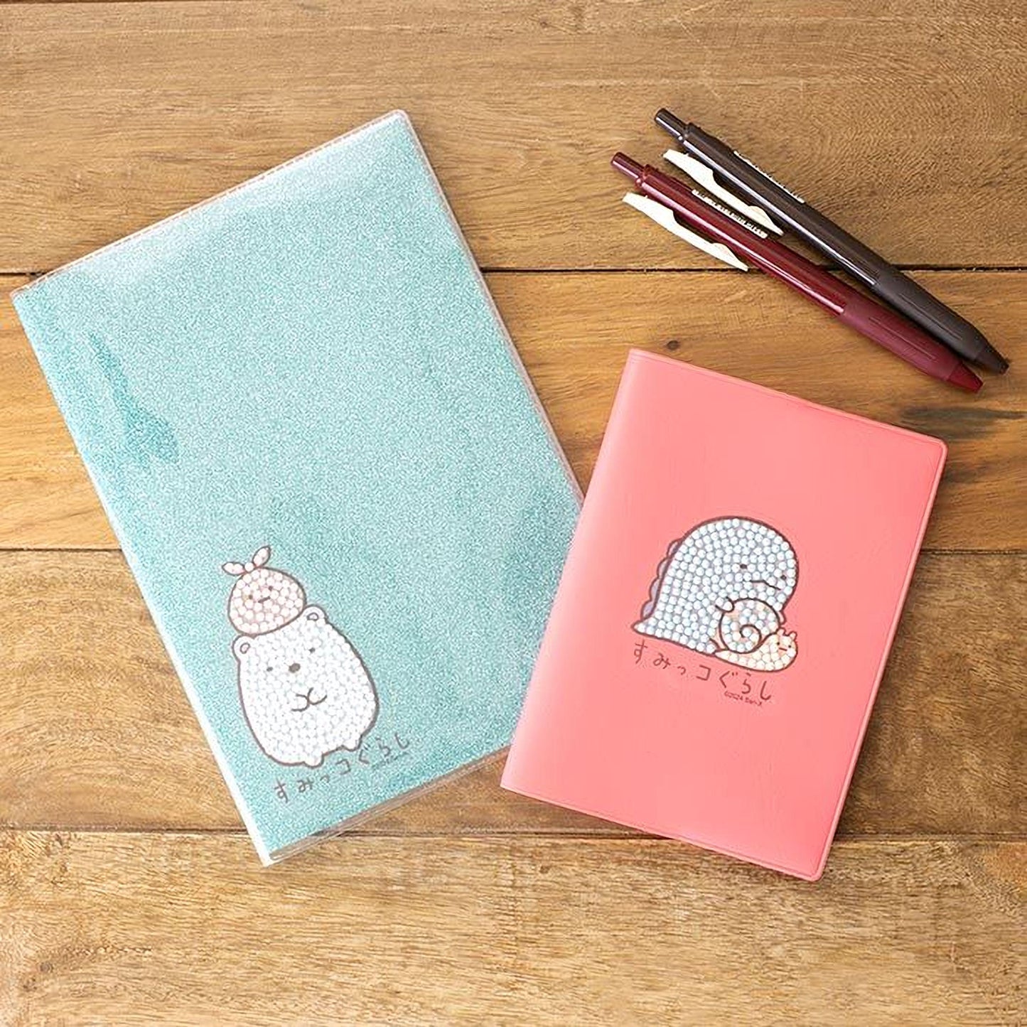 two notebooks and a pen on a wooden surface.