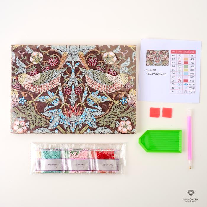 various craft supplies, including a patterned paper, a diamond tool, and a set of colored pencils, all arranged on a white background.