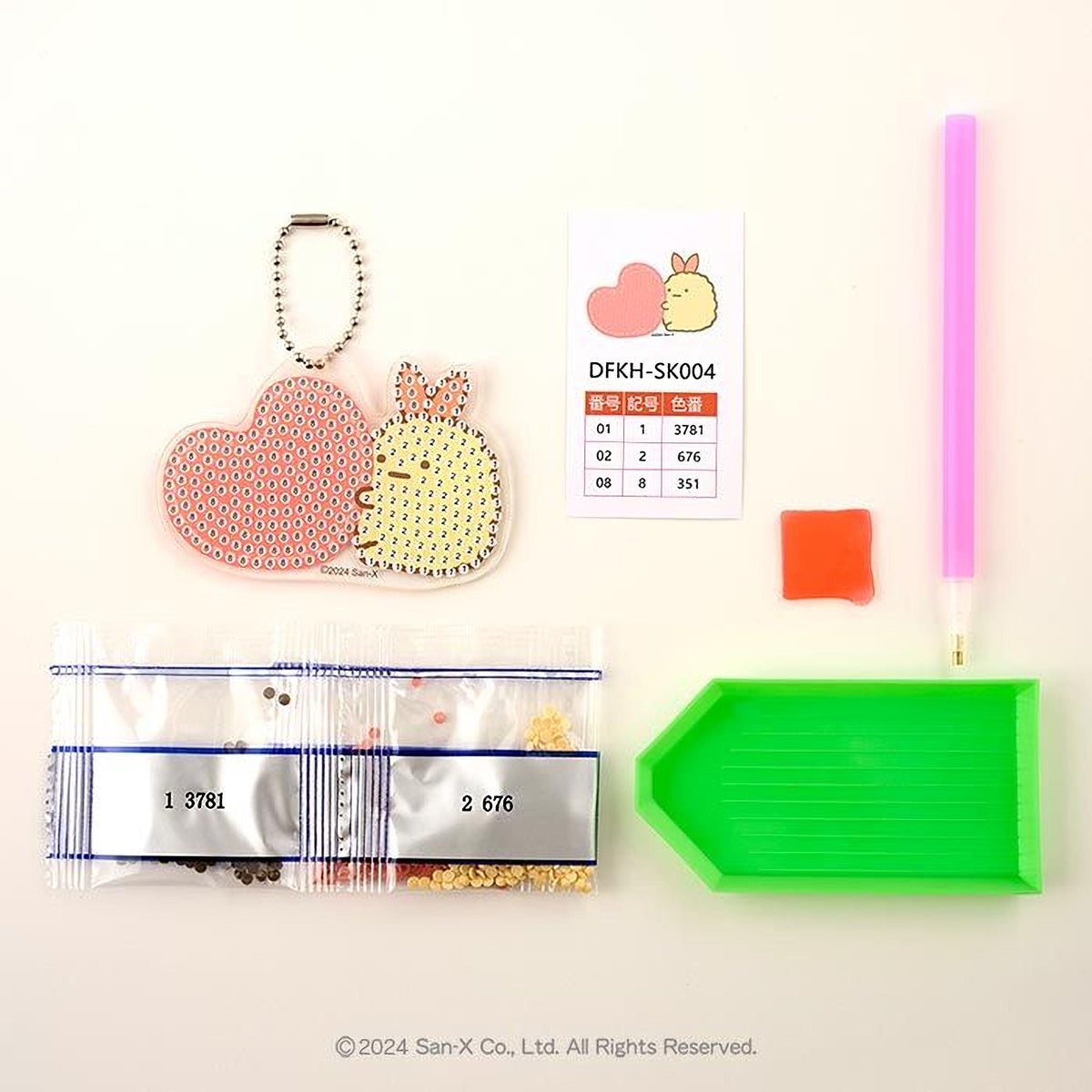 various craft supplies, including a keychain, a price list, a pen, a green tray, and a bag of beads.
