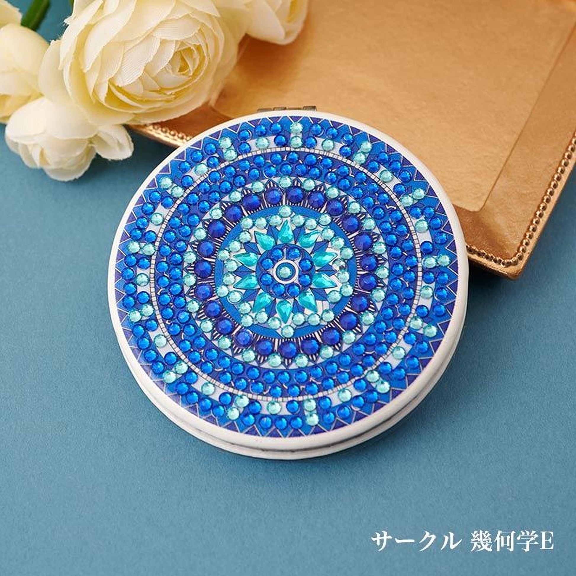 A decorative mirror with a blue and white floral pattern, placed on a blue surface next to a bouquet of white flowers.