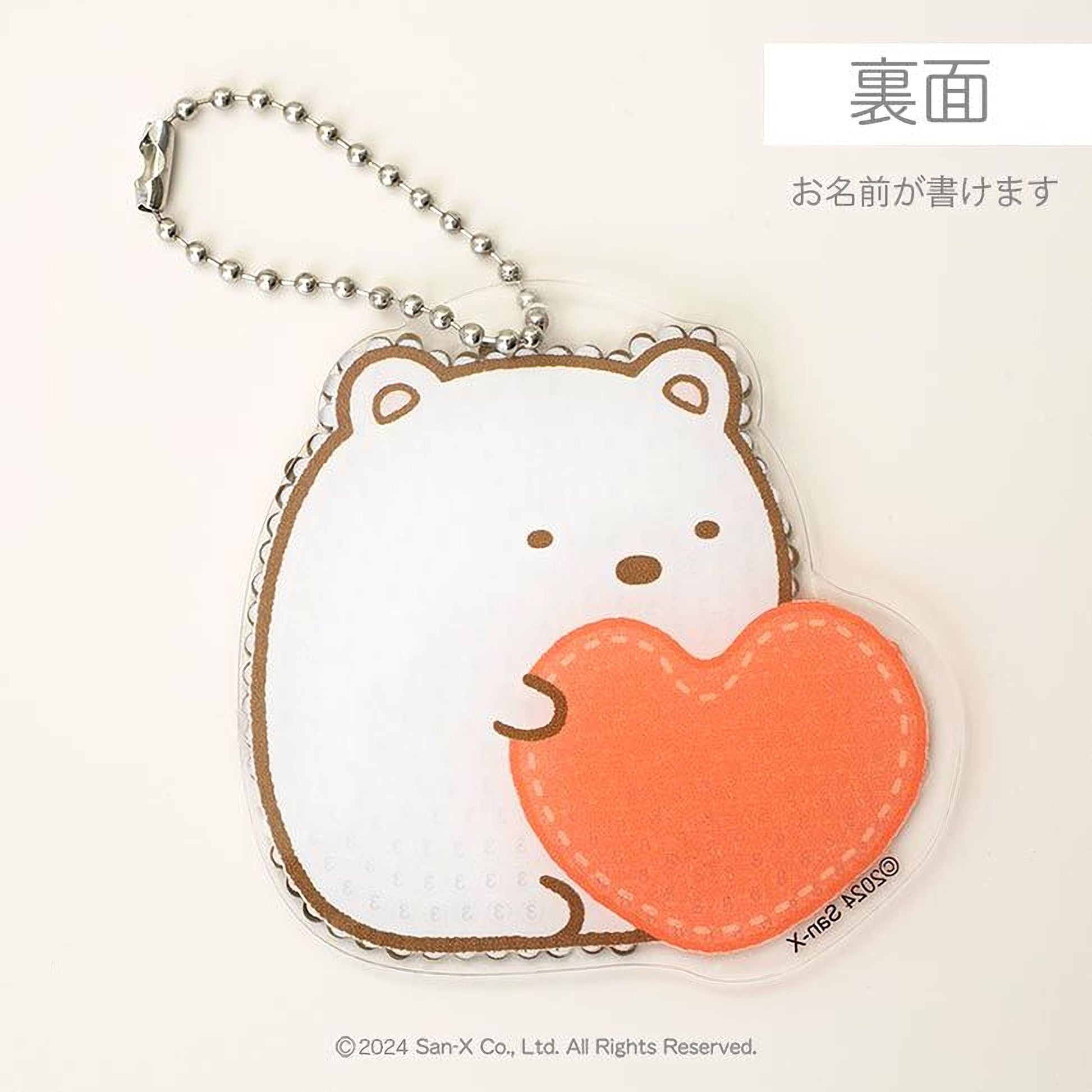 A keychain with a cute white bear holding an orange heart-shaped object.