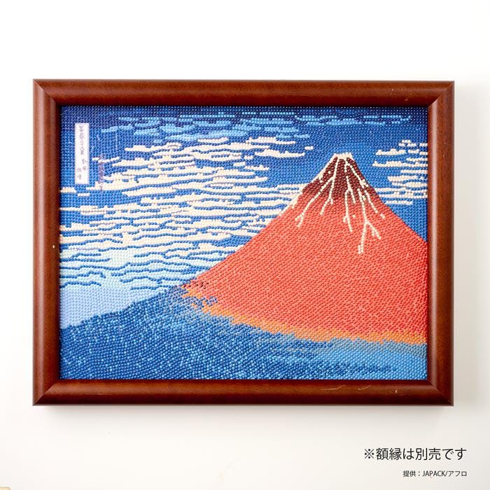 The image is a framed artwork depicting a vibrant mountain landscape with a red peak and blue sky.