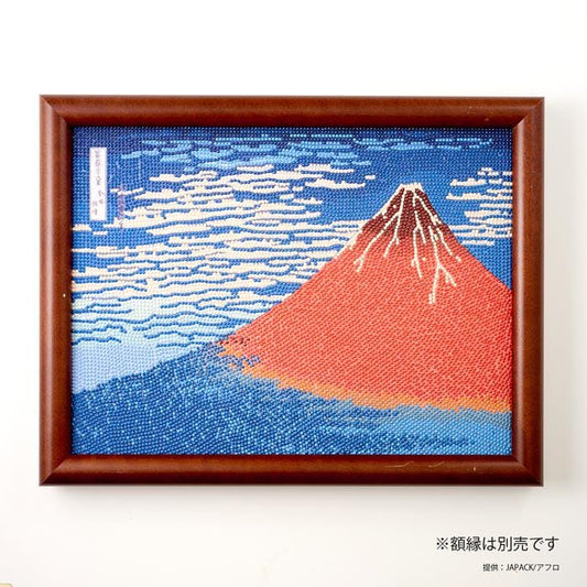 The image is a framed artwork depicting a vibrant mountain landscape with a red peak and blue sky.
