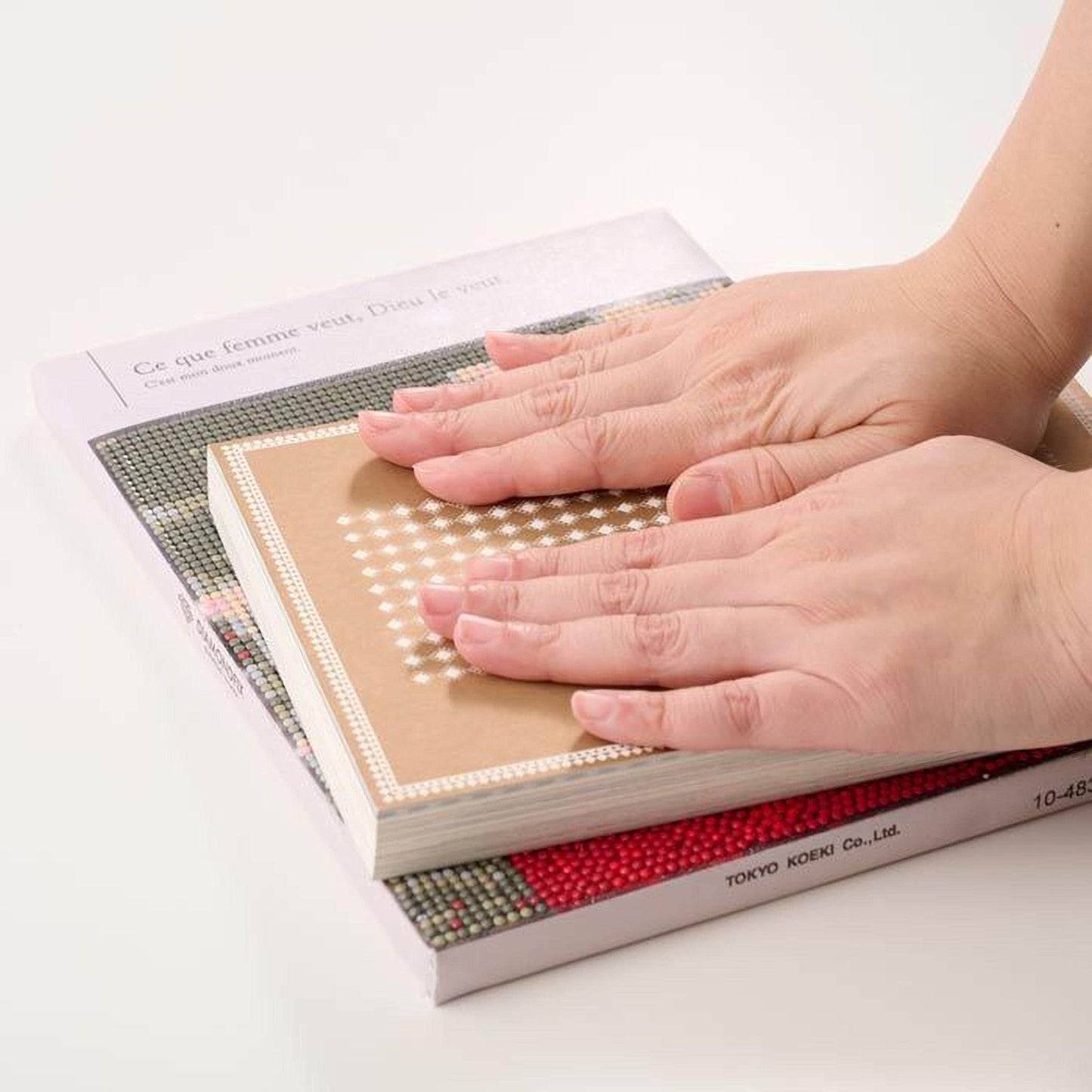 A person's hands are holding a book with a patterned cover, resting on top of another book.