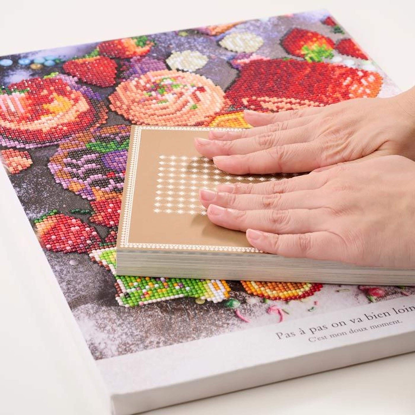 A person's hands are holding a book with a colorful, diamond-studded cover featuring a variety of fruits and flowers.