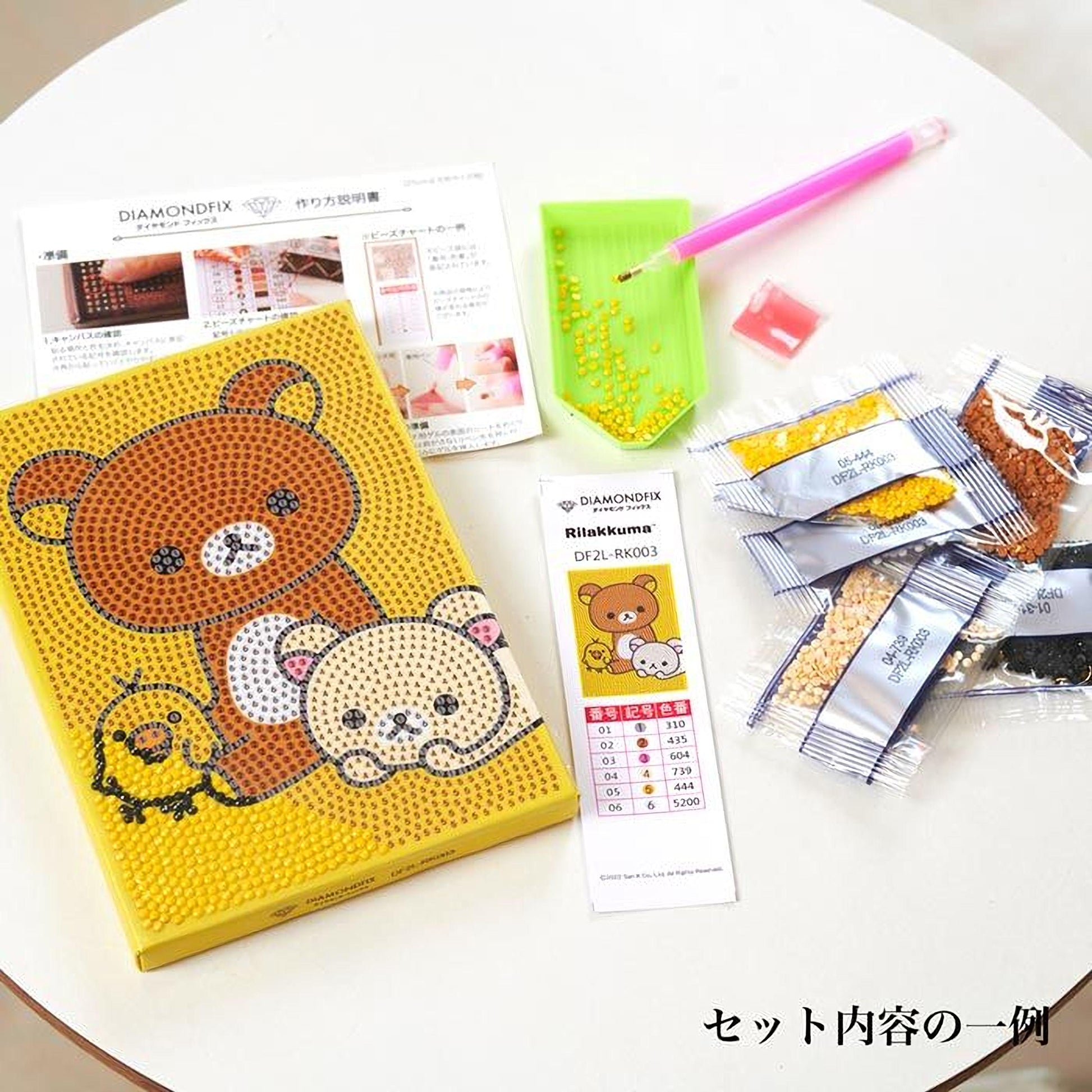 various items related to the Diamondfix brand, including a yellow box with a bear and a bird design, a green diamond pick, a pink pen, and several packages of diamond beads.
