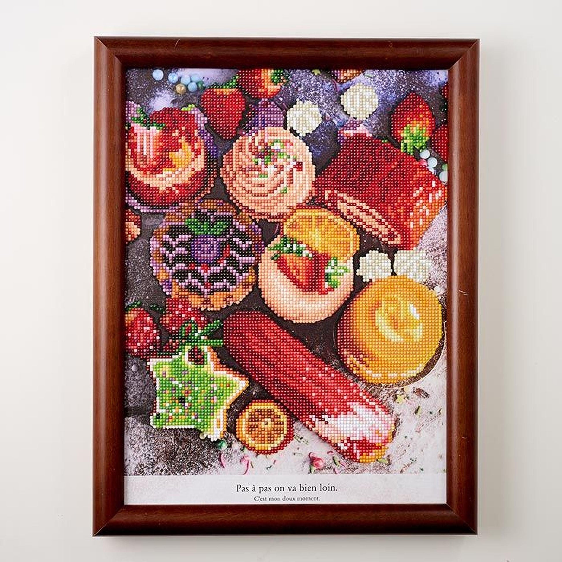 The image is a framed embroidery depicting a variety of colorful and whimsical food items, including cakes, fruits, and other desserts.