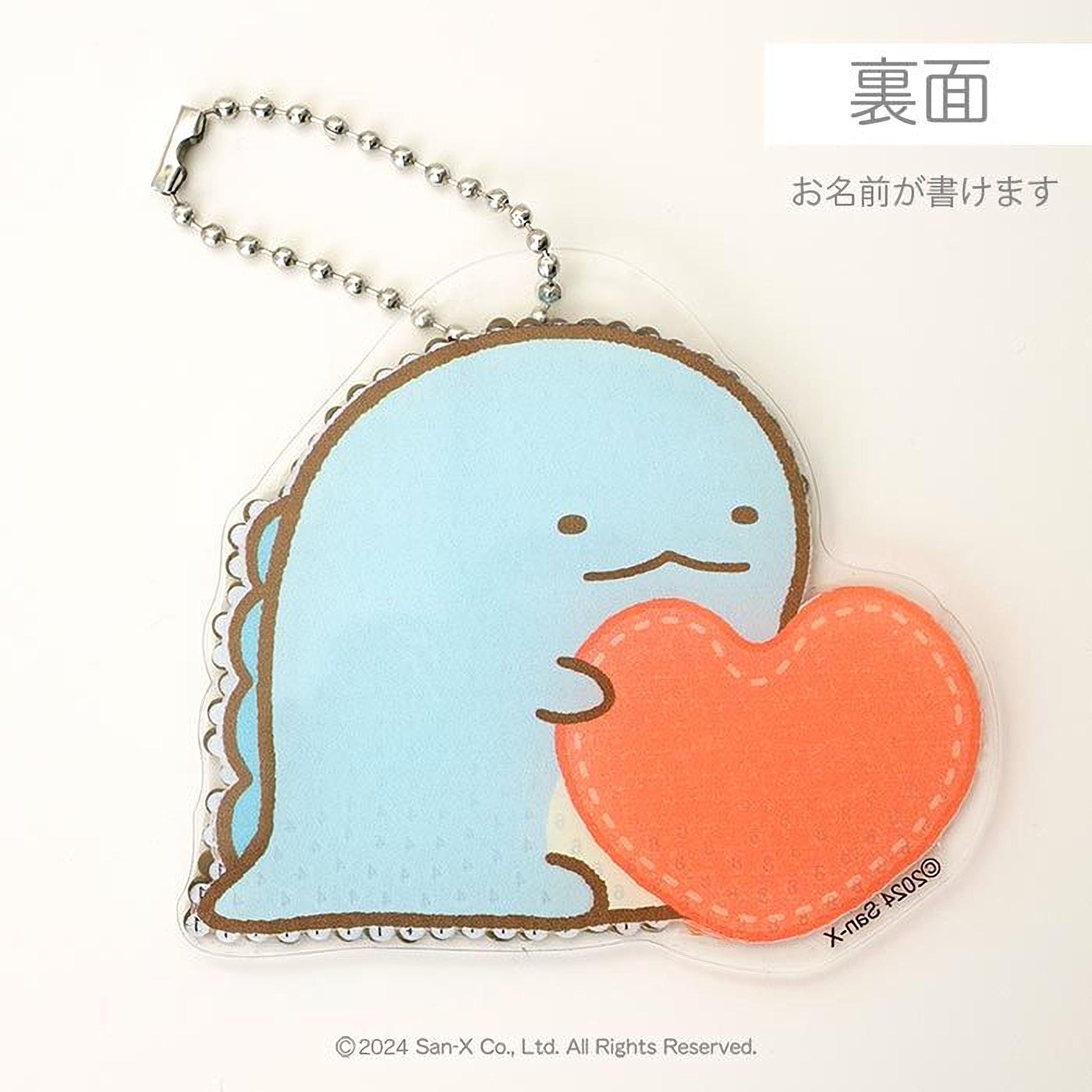 A keychain with a blue dinosaur-like character holding an orange heart-shaped object.