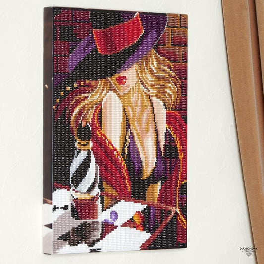 The image is a diamond-studded embroidery or cross-stitch artwork depicting a woman wearing a purple hat and a red dress, with a bottle of perfume in the background.