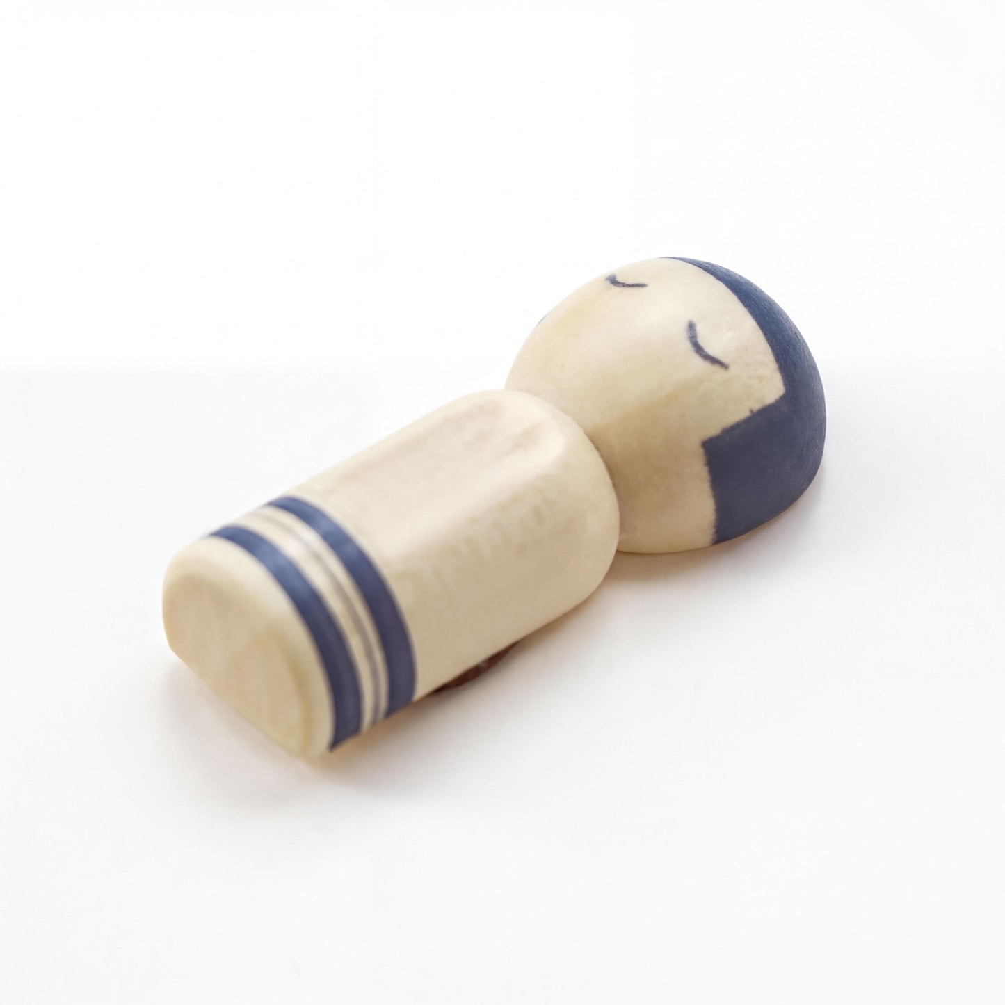 A wooden doll with a blue headband and striped body is lying down on a white surface.