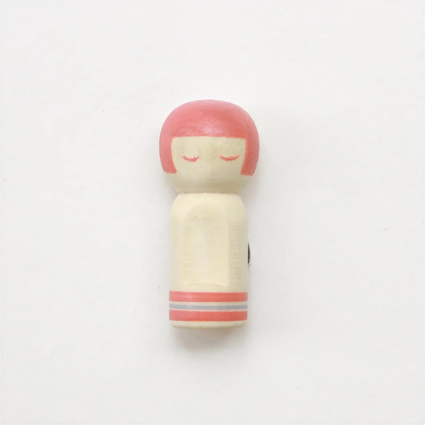 A small wooden doll with a pink head and red eyes is shown against a plain white background.