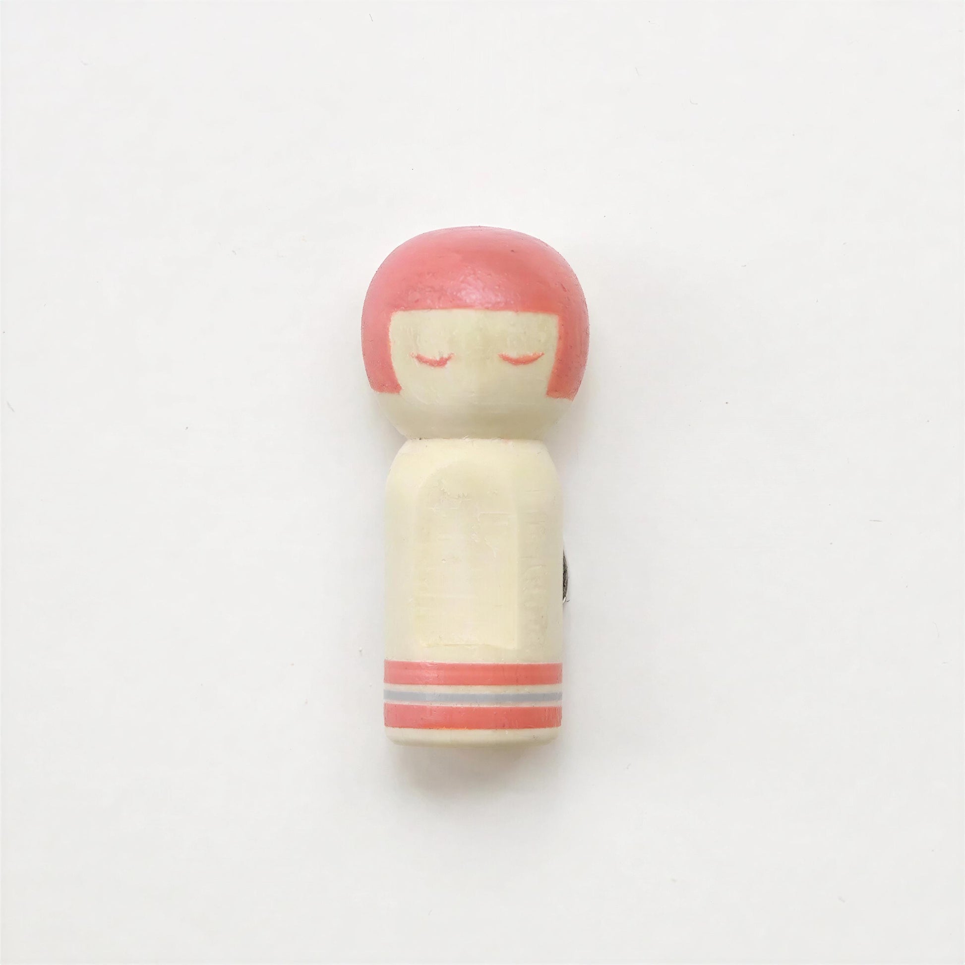 A small wooden doll with a pink head and red eyes is shown against a plain white background.