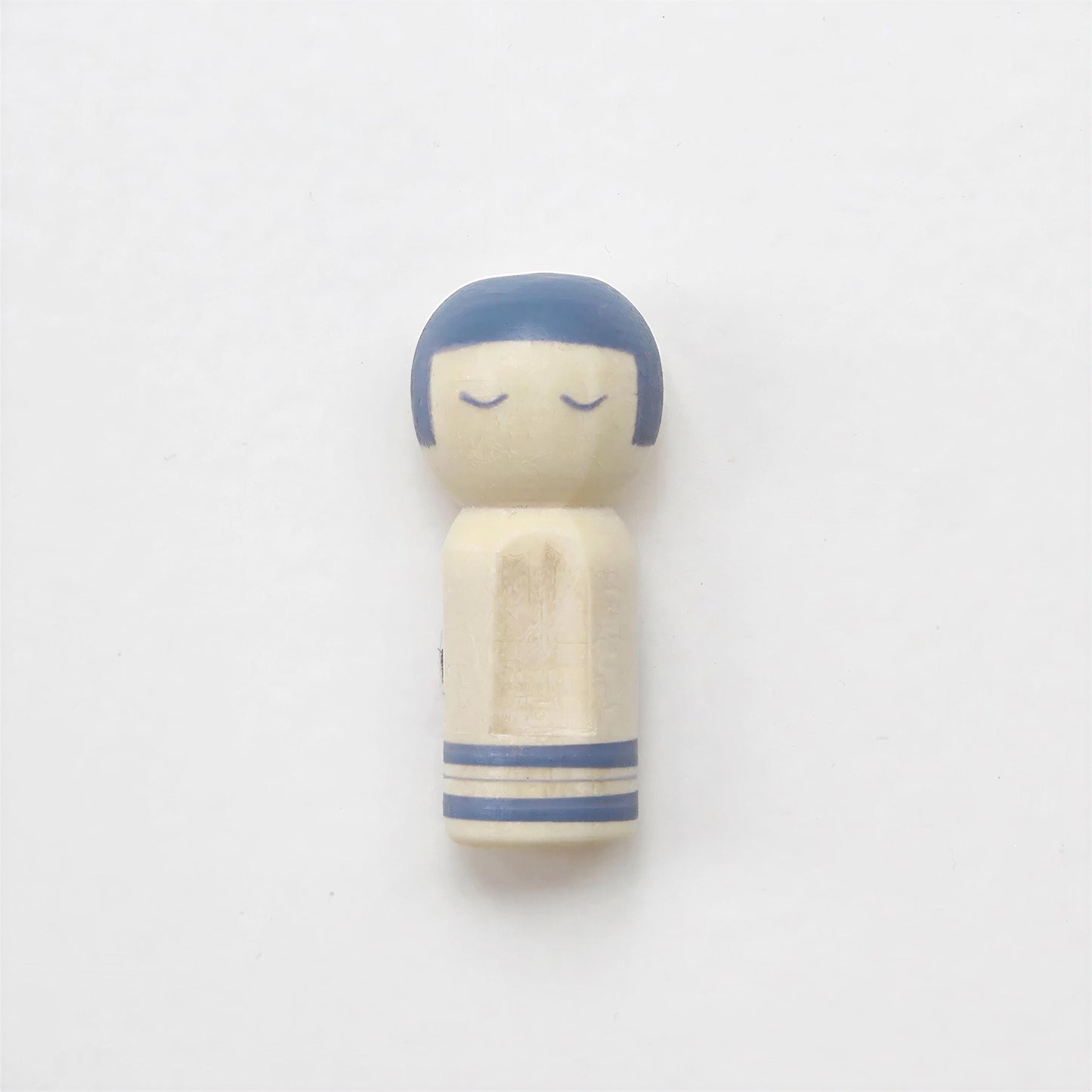 A small wooden figurine with a blue head and arms, sitting on a plain white background.