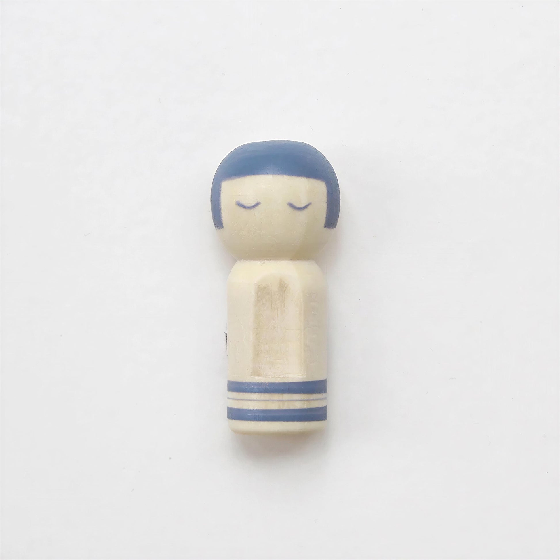 A small wooden figurine with a blue head and arms, sitting on a plain white background.