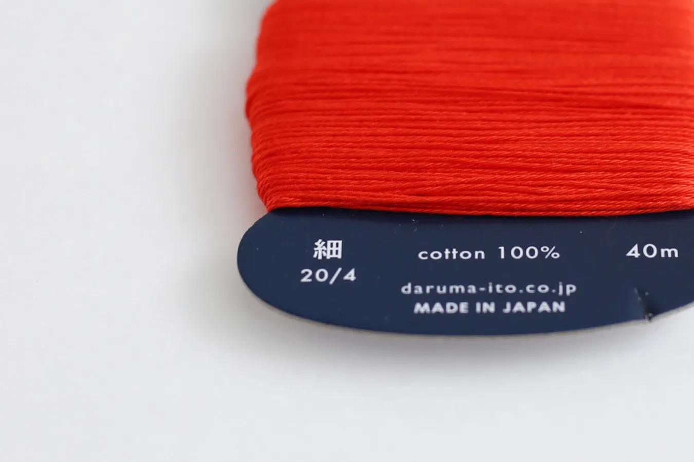 a spool of red thread with a label indicating the cotton content and the manufacturer's information.