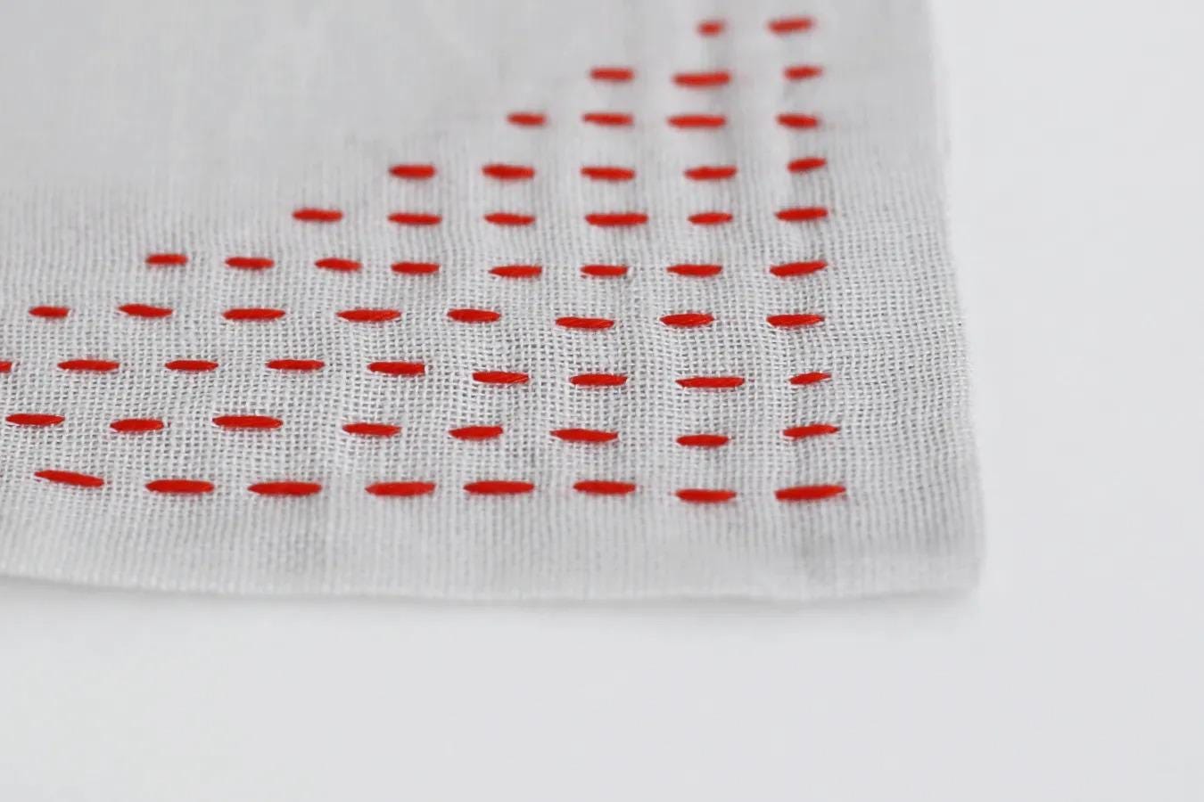 a close-up view of a white fabric with red embroidered dots arranged in a diagonal pattern.